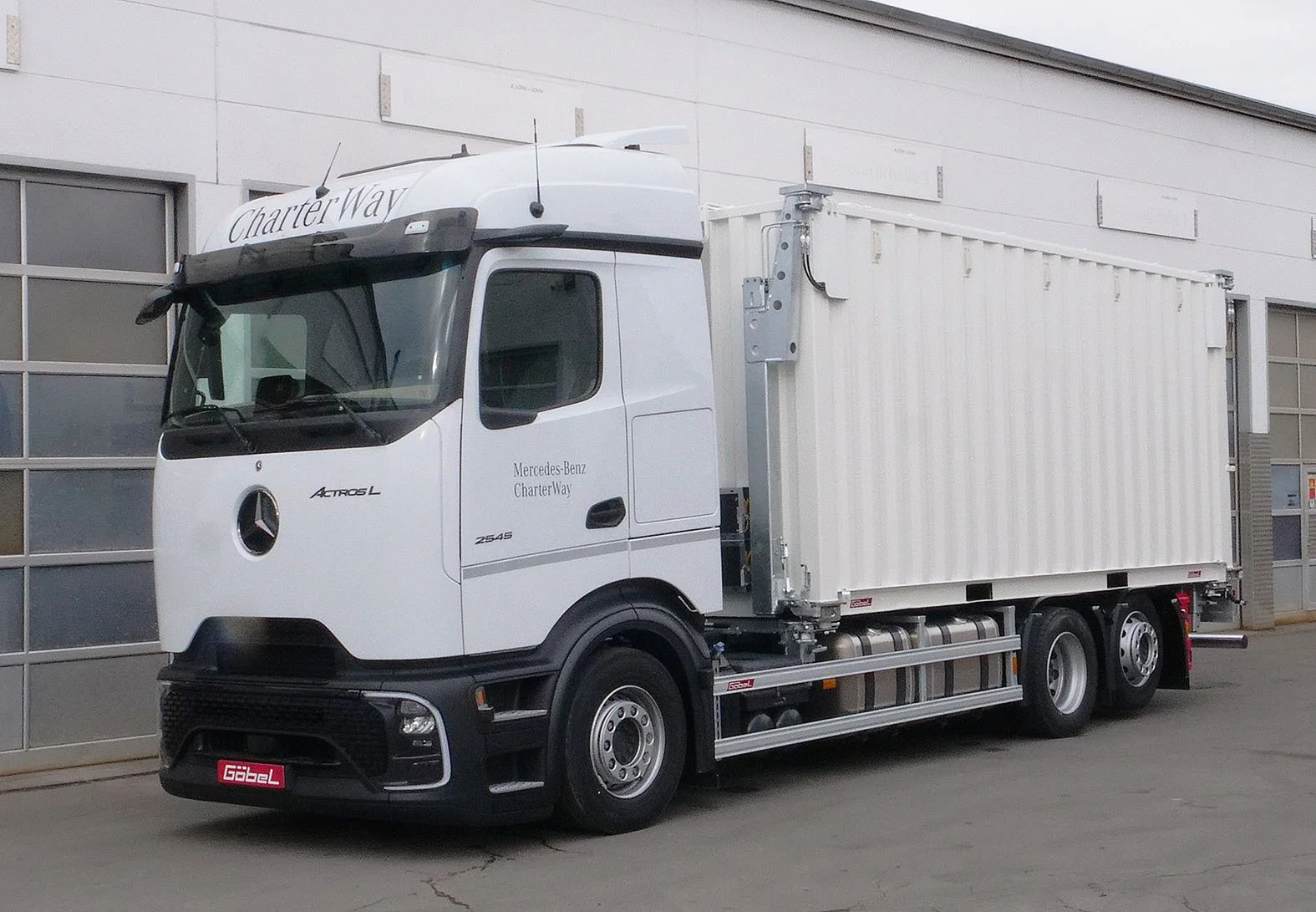 Ein Mercedes-Benz Actros L Lastwagen mit einem weißen Frachtcontainer, parkiert neben einer modernen Lagerhalle.