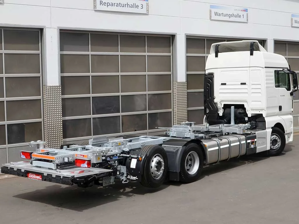 Leeres LKW-Chassis vor einem Werkstattgebäude.