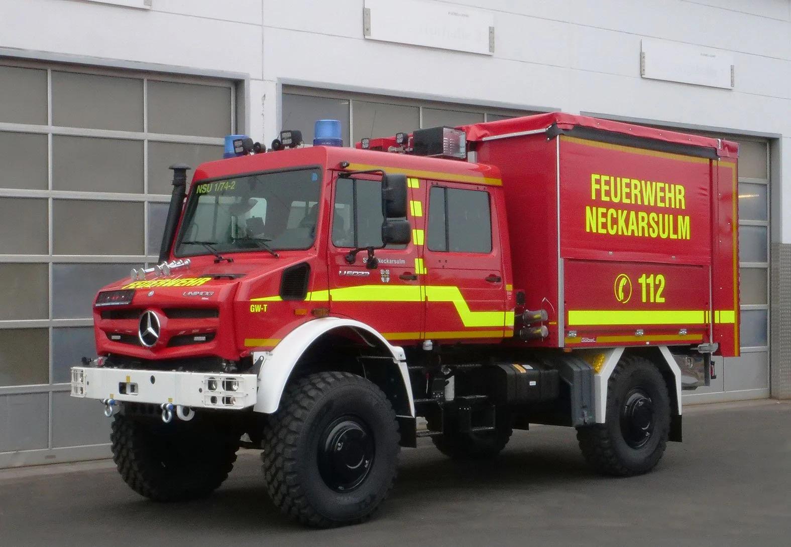 Rotes Feuerwehrfahrzeug der Feuerwehr Neckarsulm mit Gelblicher Beschriftung und Einsatznummern, vor einer Garage.