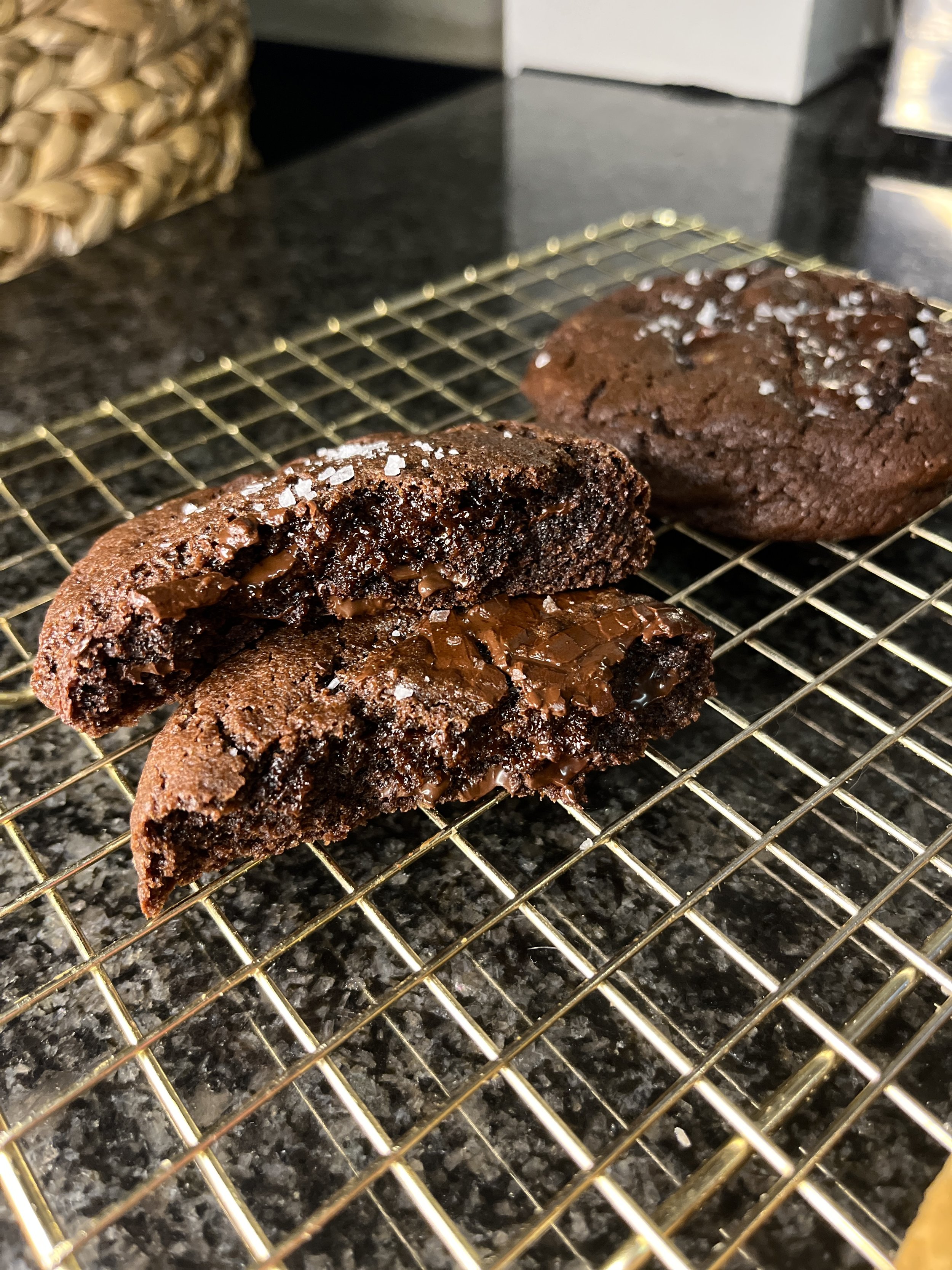 Segmjuka mörka hokladkakor på ett avsvalningsgaller, en av dem är delvis uppbruten för att visa den kladdiga insidan.