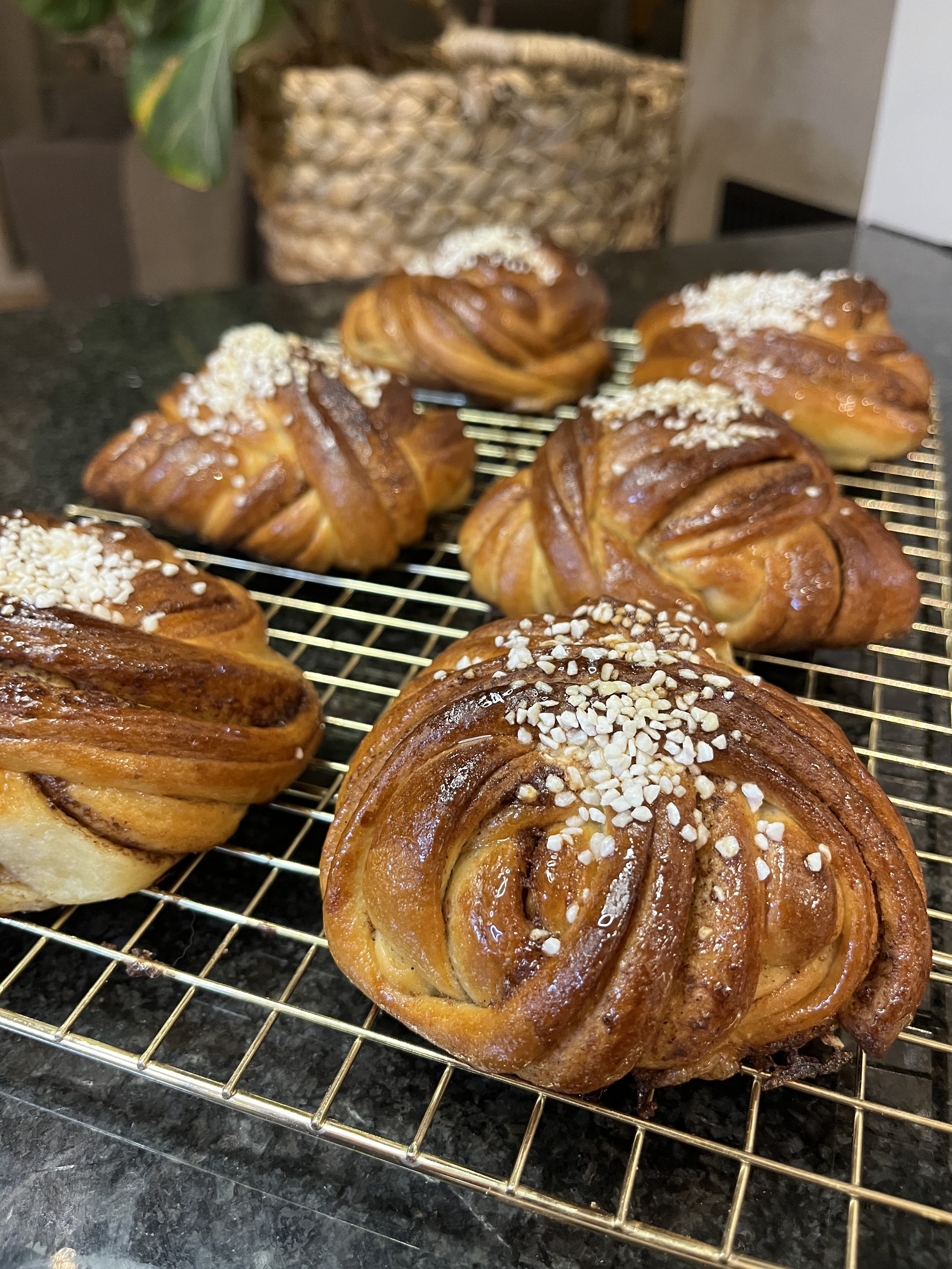 Stora saftiga kanelbullar av surdeg, toppade med pärlsocker, placerade på ett galler.