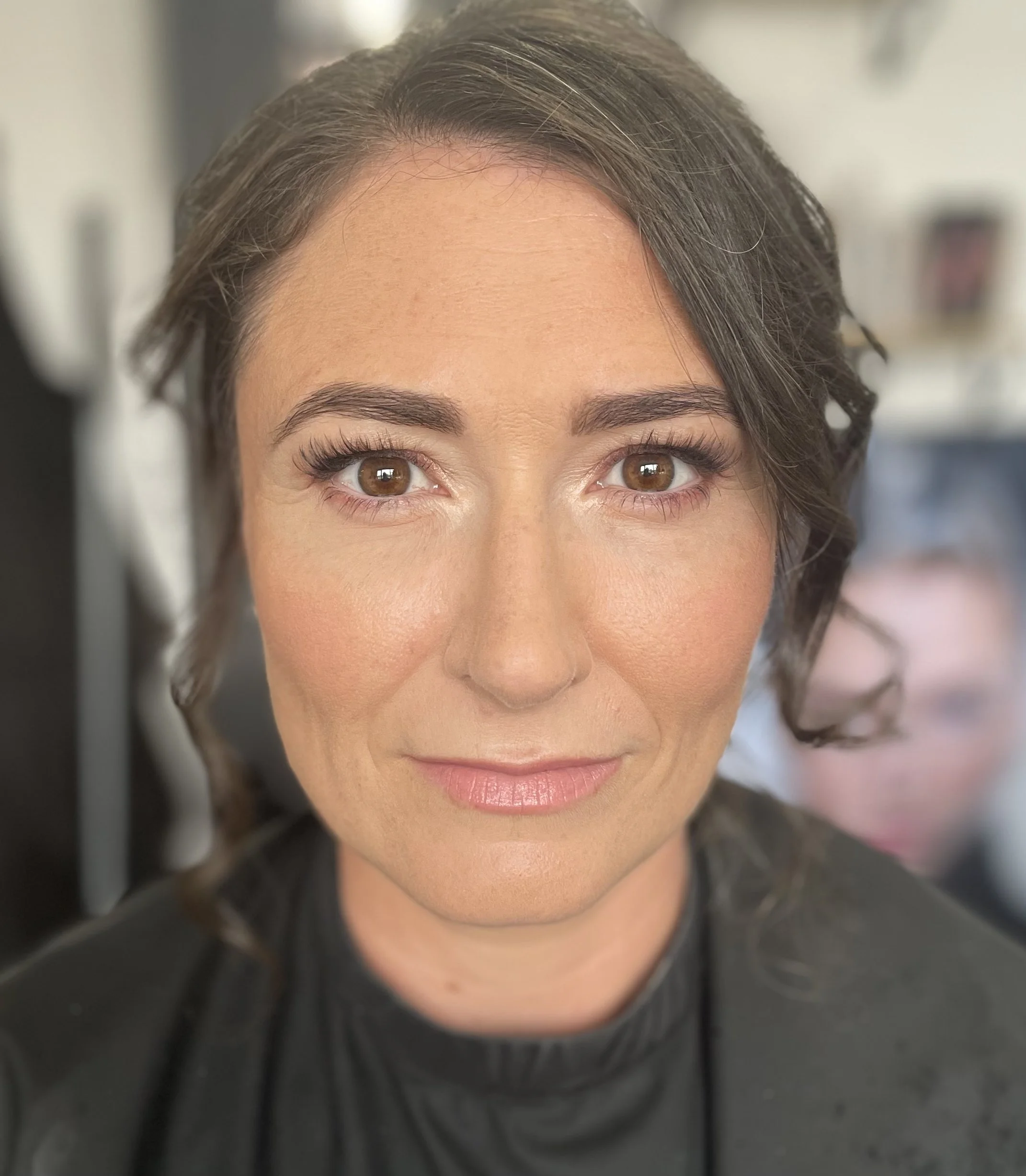 A close-up of a woman's face showing her brown eyes, eyebrows, nose, and part of her forehead and cheeks. Her hair is curly and brown, framing her face.