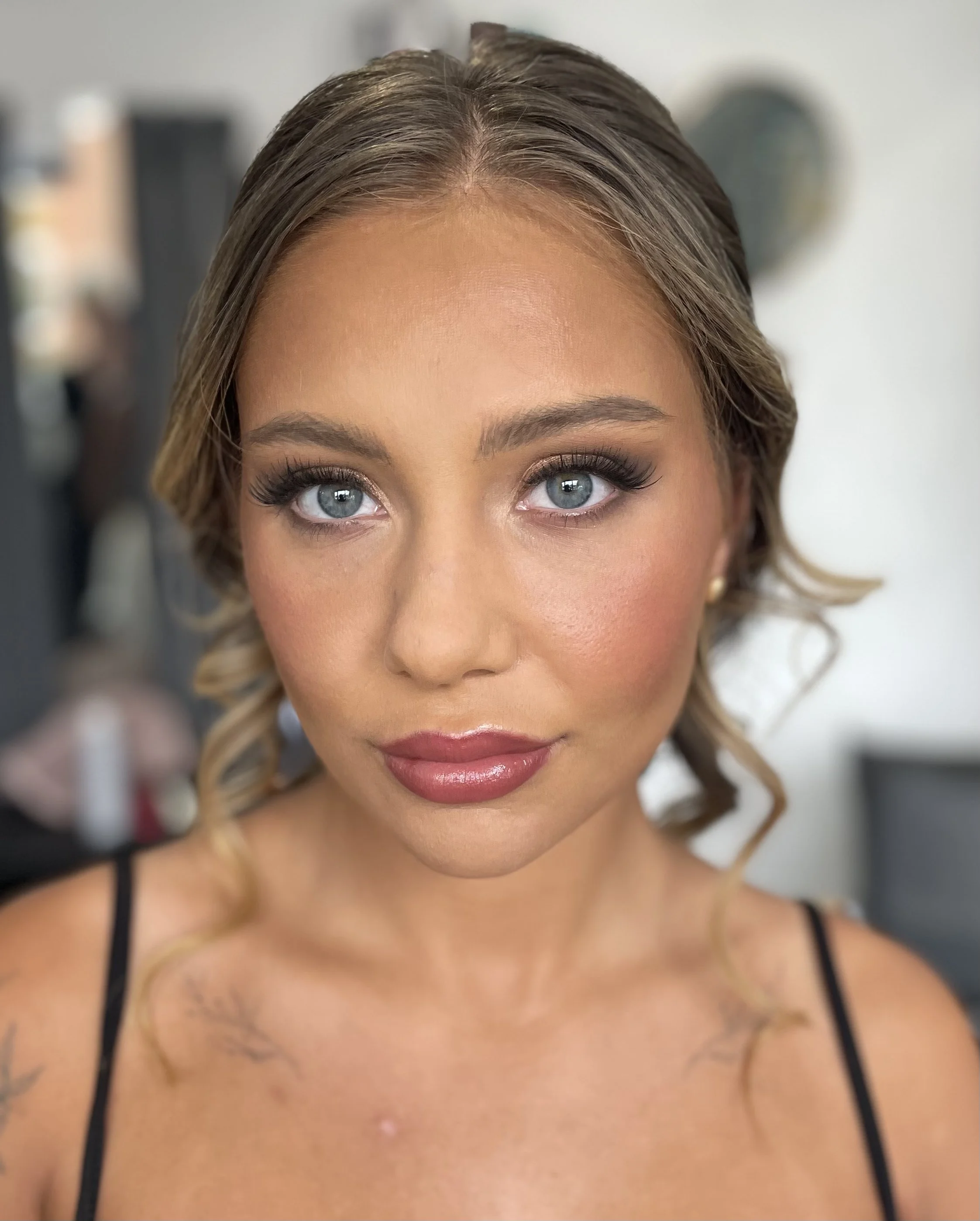 Close-up of a woman's face showing her eyes, nose, and part of her lips, with makeup, jewelry, and a black strap dress, in a portrait style.