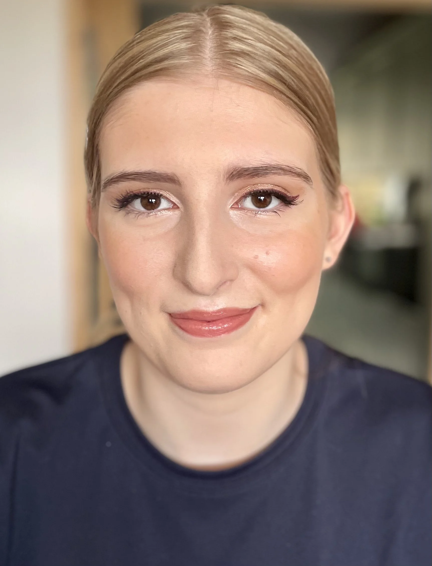 Close-up of a woman's face showing her smiling lips, nose, and brown eyes, with groomed eyebrows and light makeup, wearing a dark top.