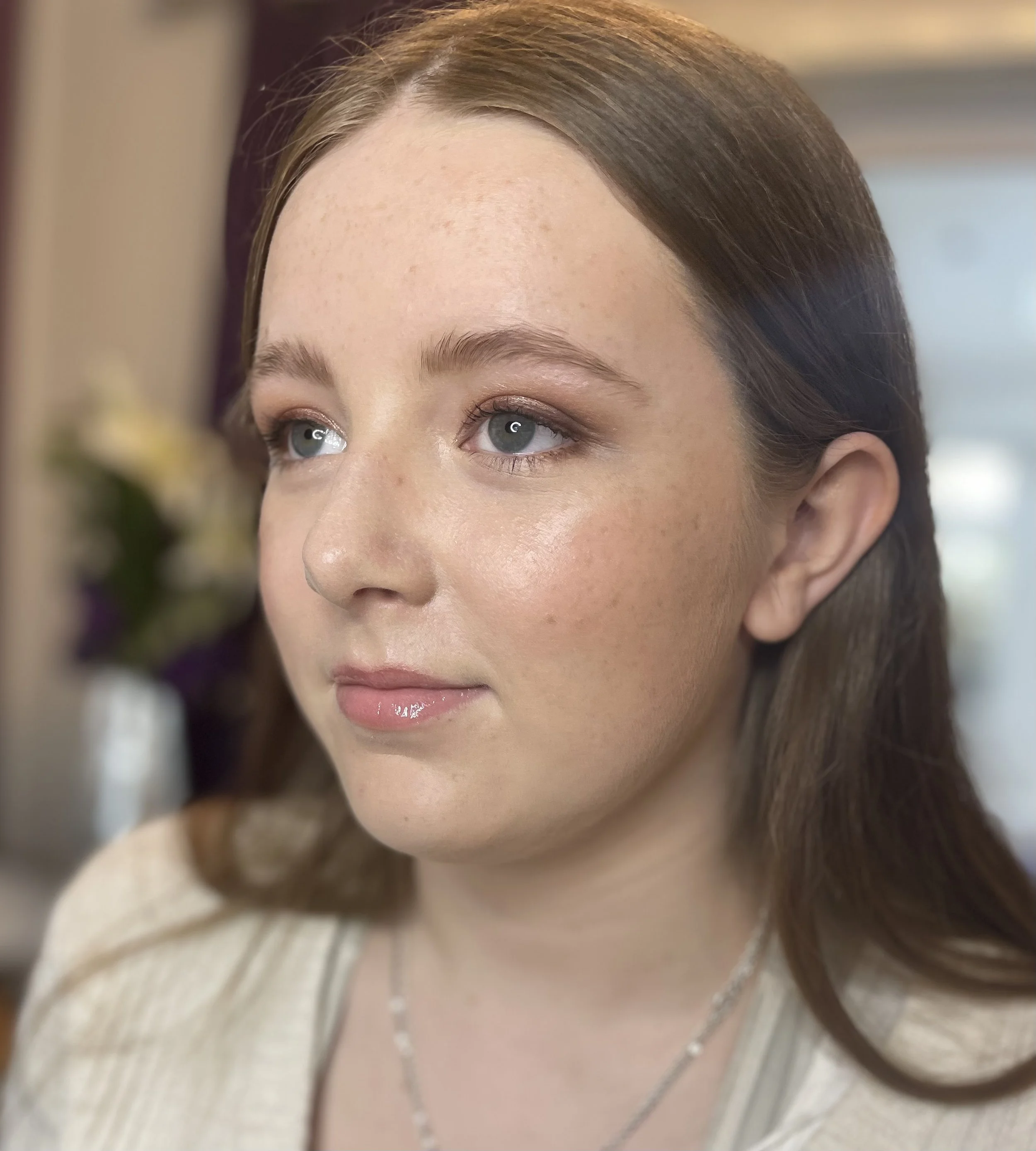 Close-up of a young woman's face showing a natural and glowing makeup that looks skin like. She has light blue eyes, light brown hair, and light skin.