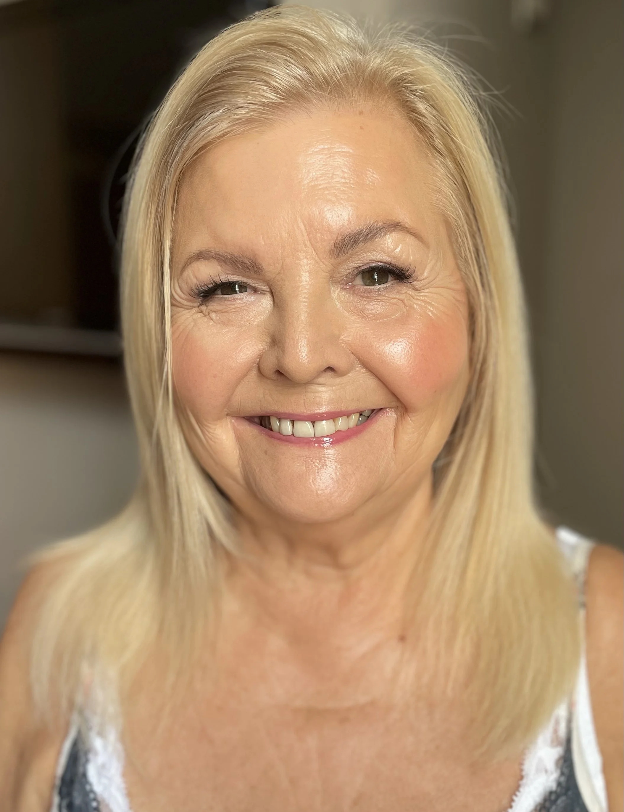 Close-up of a smiling mature woman with blonde hair, showing her face, eyes, and teeth.