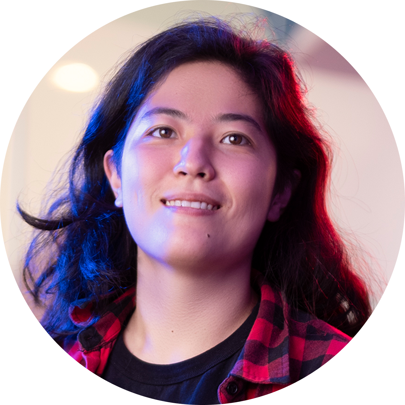 Portrait of a person with long black hair wearing a red and black checkered shirt, illuminated by colorful lighting.