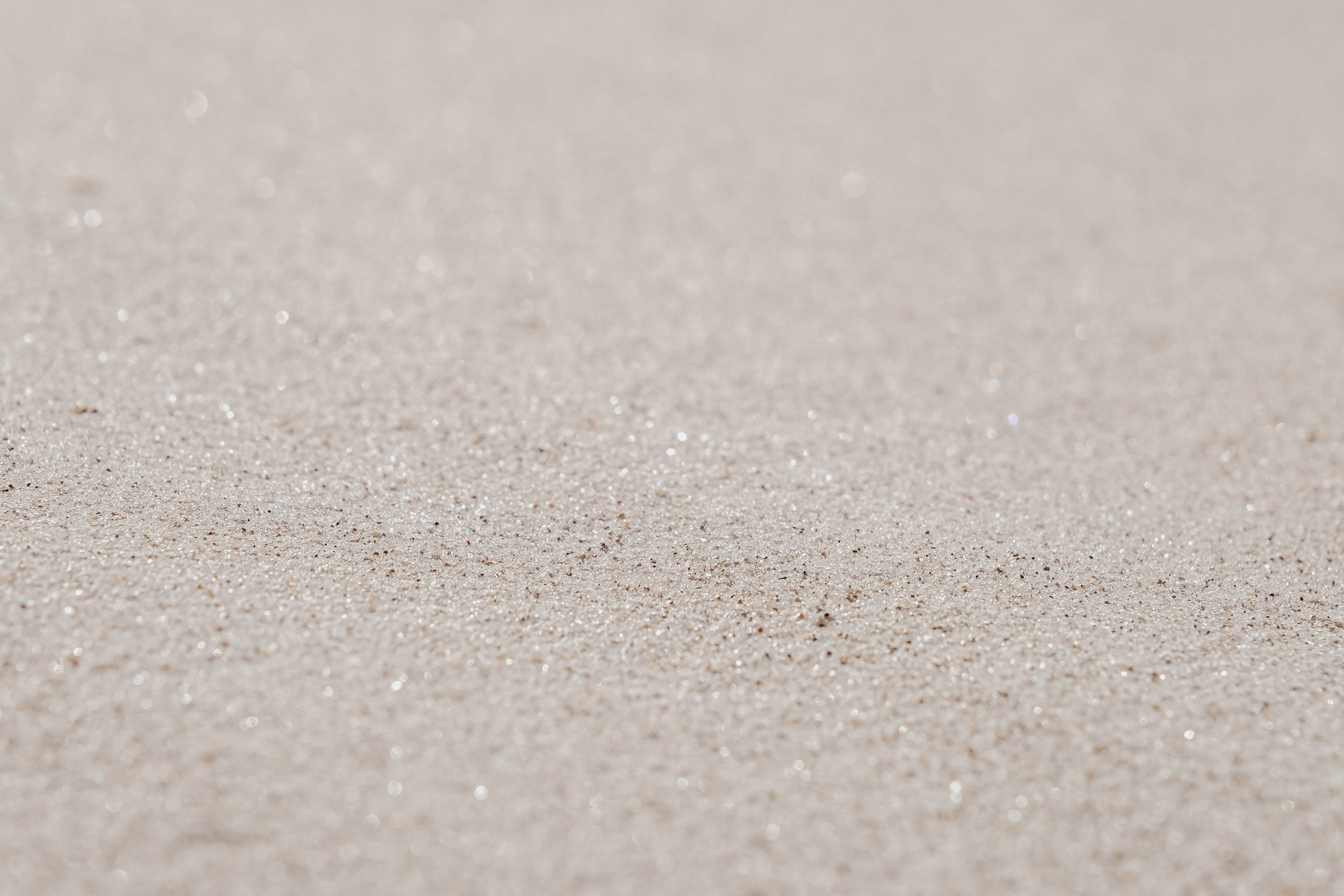 Close-up of a sandy beach surface with fine, light-colored sand and a few tiny sparkles.
