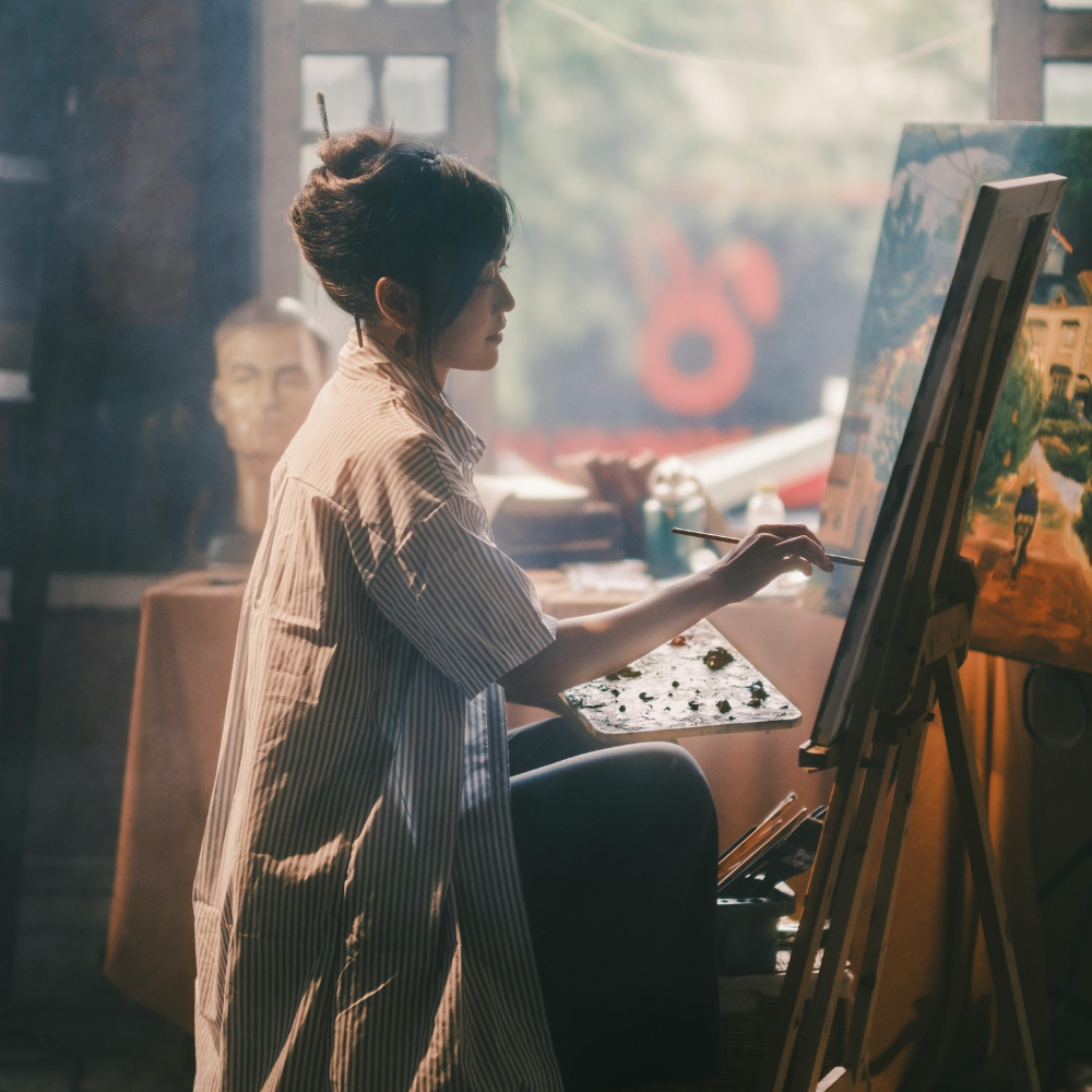 A woman painting on a canvas in an art studio with sunlight streaming in.