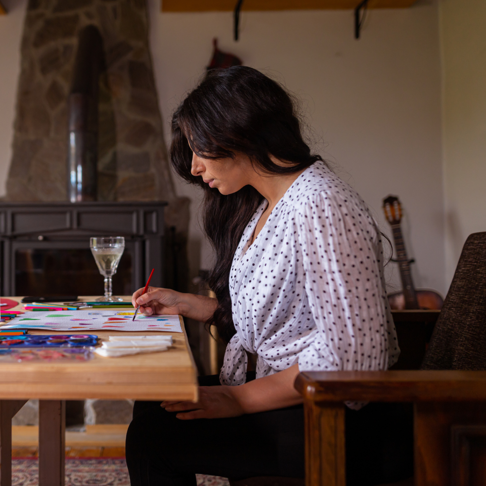 Woman painting colorful patterns on paper at a wooden table.