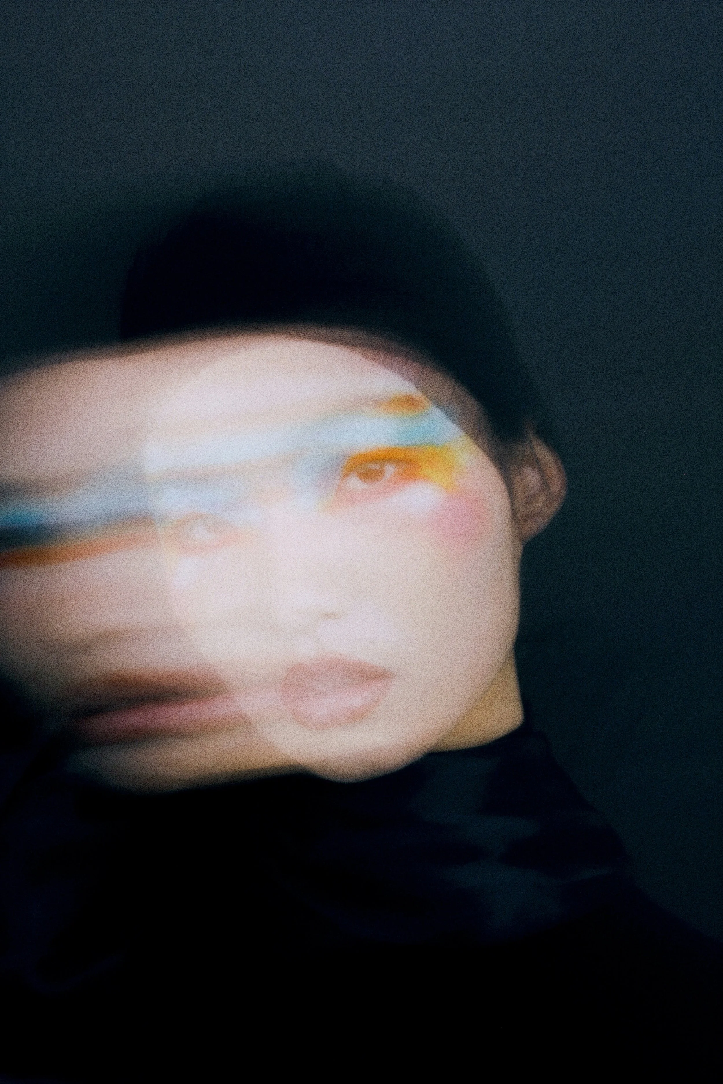 Close-up of a mannequin's face with makeup, partially obscured by a dark hat, against a dark background.