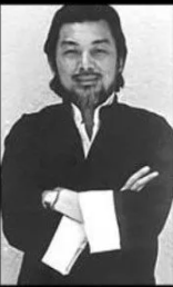 Black and white photo of a man with arms crossed, wearing a dark jacket with white cuffs.