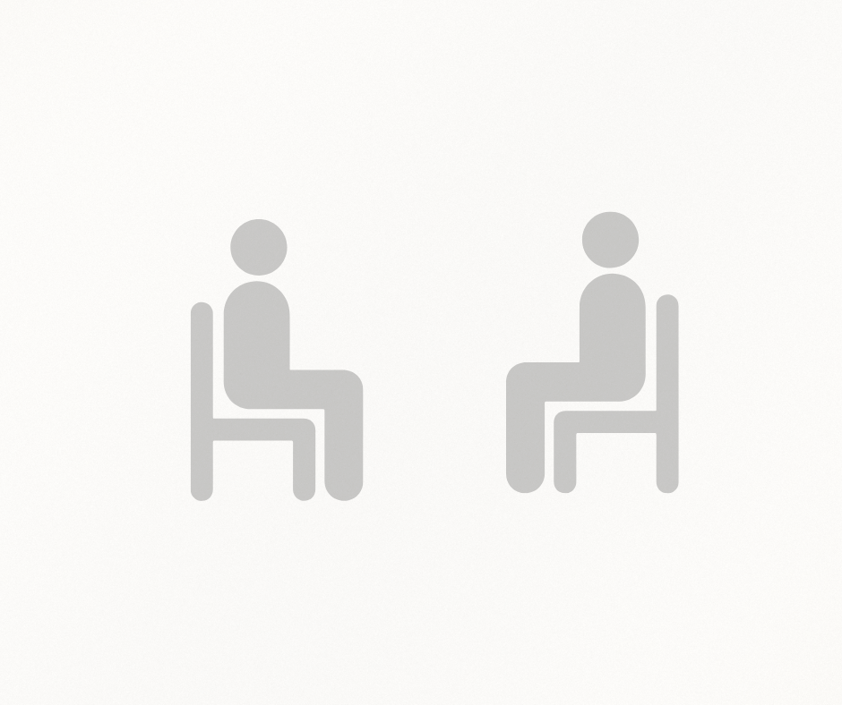 Two simplistic gray icons of people sitting on chairs facing each other on a white background.