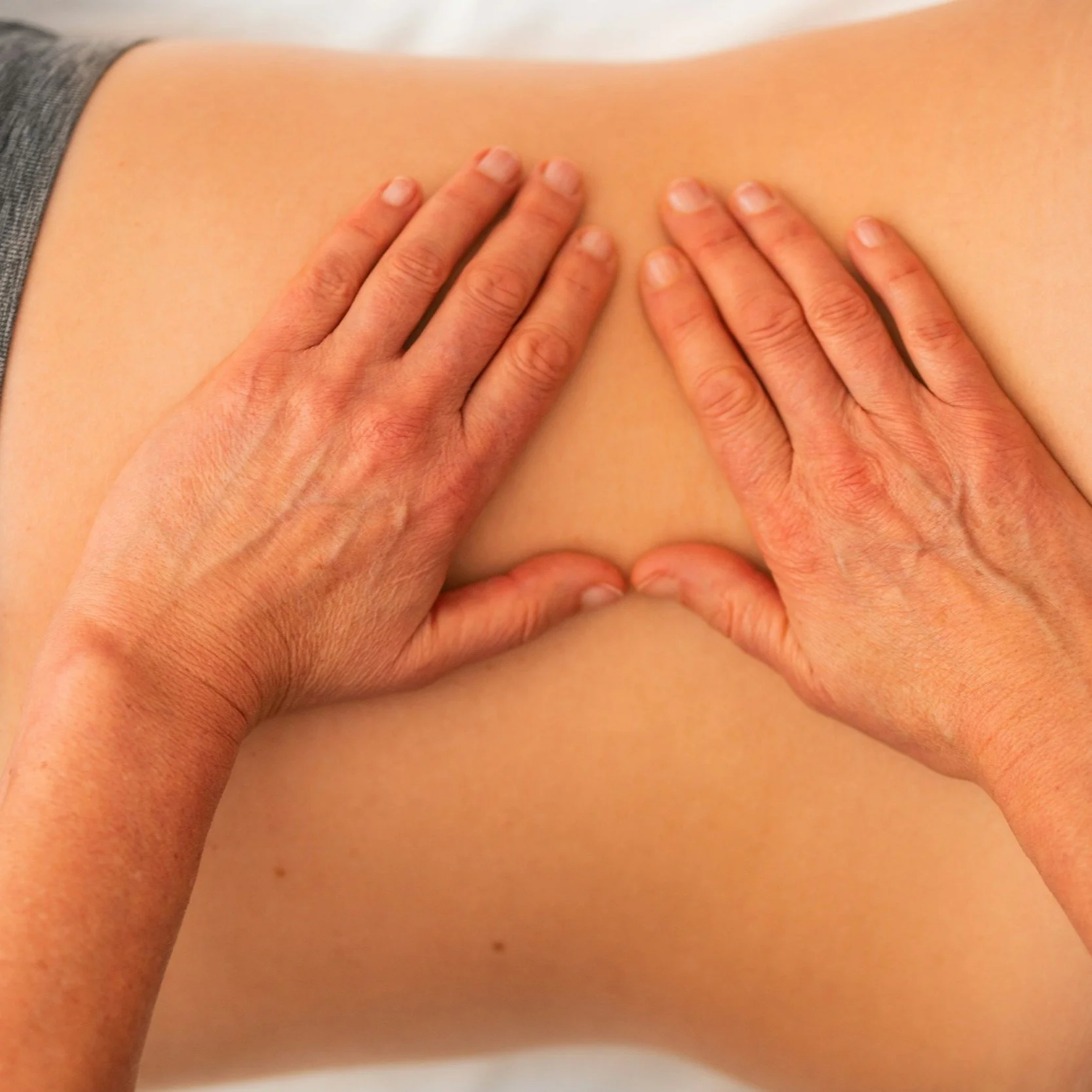 Two hands pressing on a person's back during a massage.