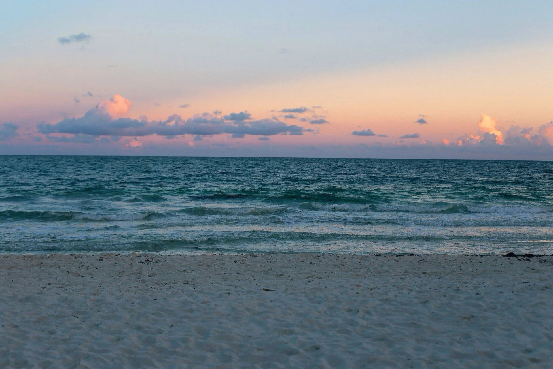 Beach scene with sandy shore, gentle waves, and a colorful sky with pink and orange clouds at sunset.