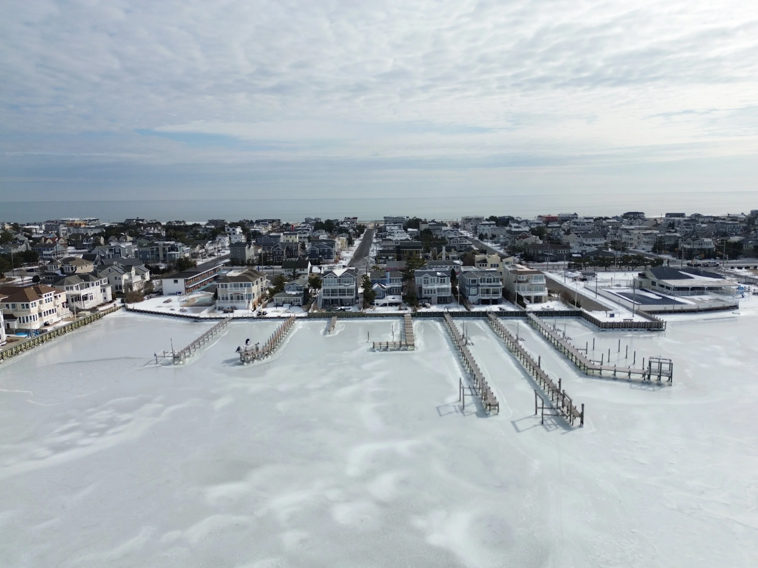 A frozen bay on Long Beach Island with large beach houses in the background