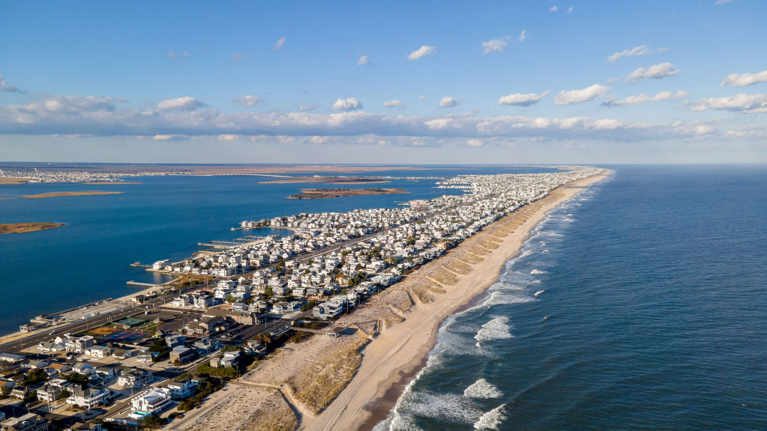 Aerial view of a coastal long beach island, nj, and the atlantic ocean to the left under a partly cloudy sky.