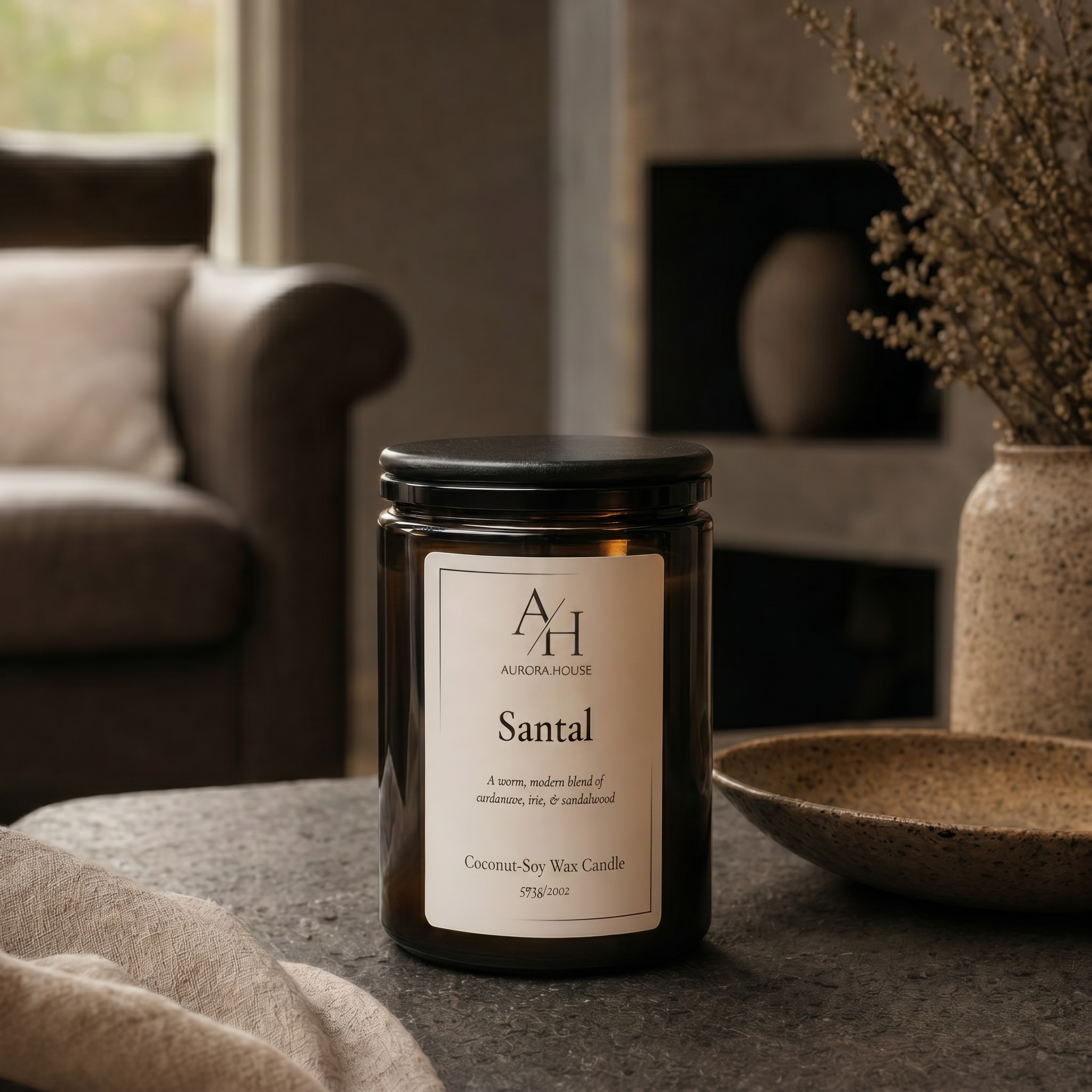 Large luxury Aurora House 20oz Santal candle styled on a dark stone coffee table in a modern moody living room with warm ambient lighting and minimalist decor.