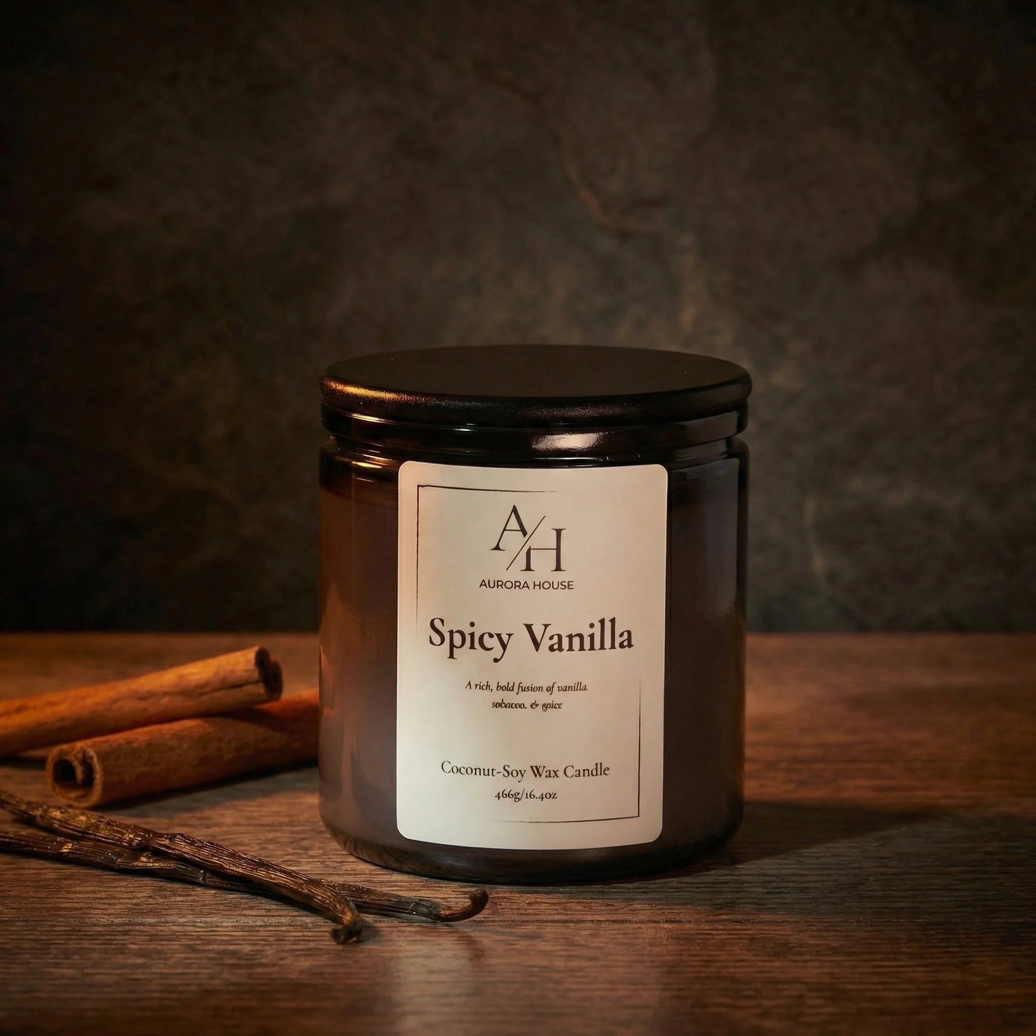 A black candle jar labeled 'Aurora House Spicy Vanilla' with cinnamon sticks and star anise nearby on a light gray surface.