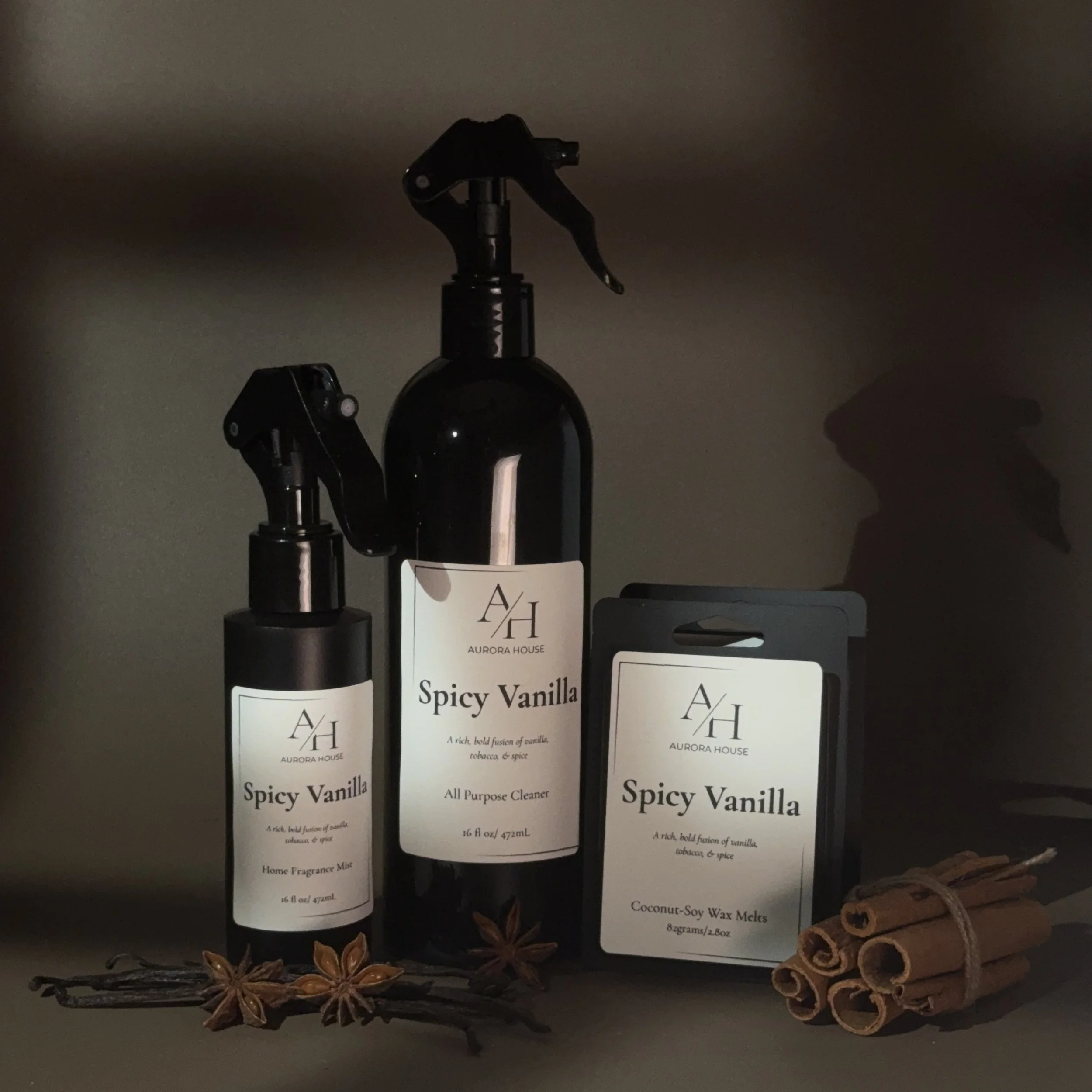 Bathroom shelf display of Aurora House Spicy Vanilla products including a home fragrance mist, all-purpose cleaner, and coconut-soy wax melts, with cinnamon sticks and star anise.
