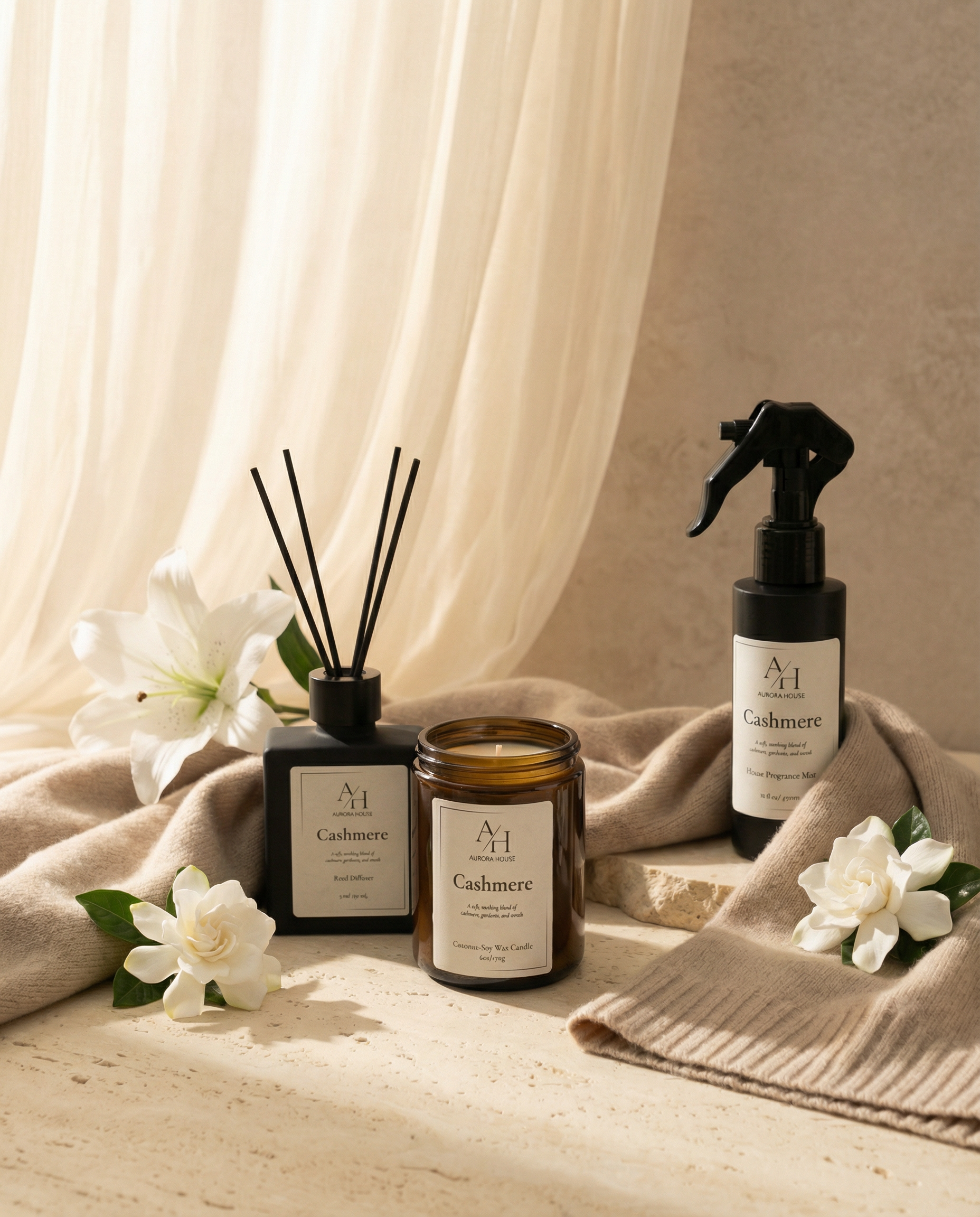 Cashmere candle, reed diffuser, and fragrance mist styled on warm neutral stone with white florals and knit fabric.