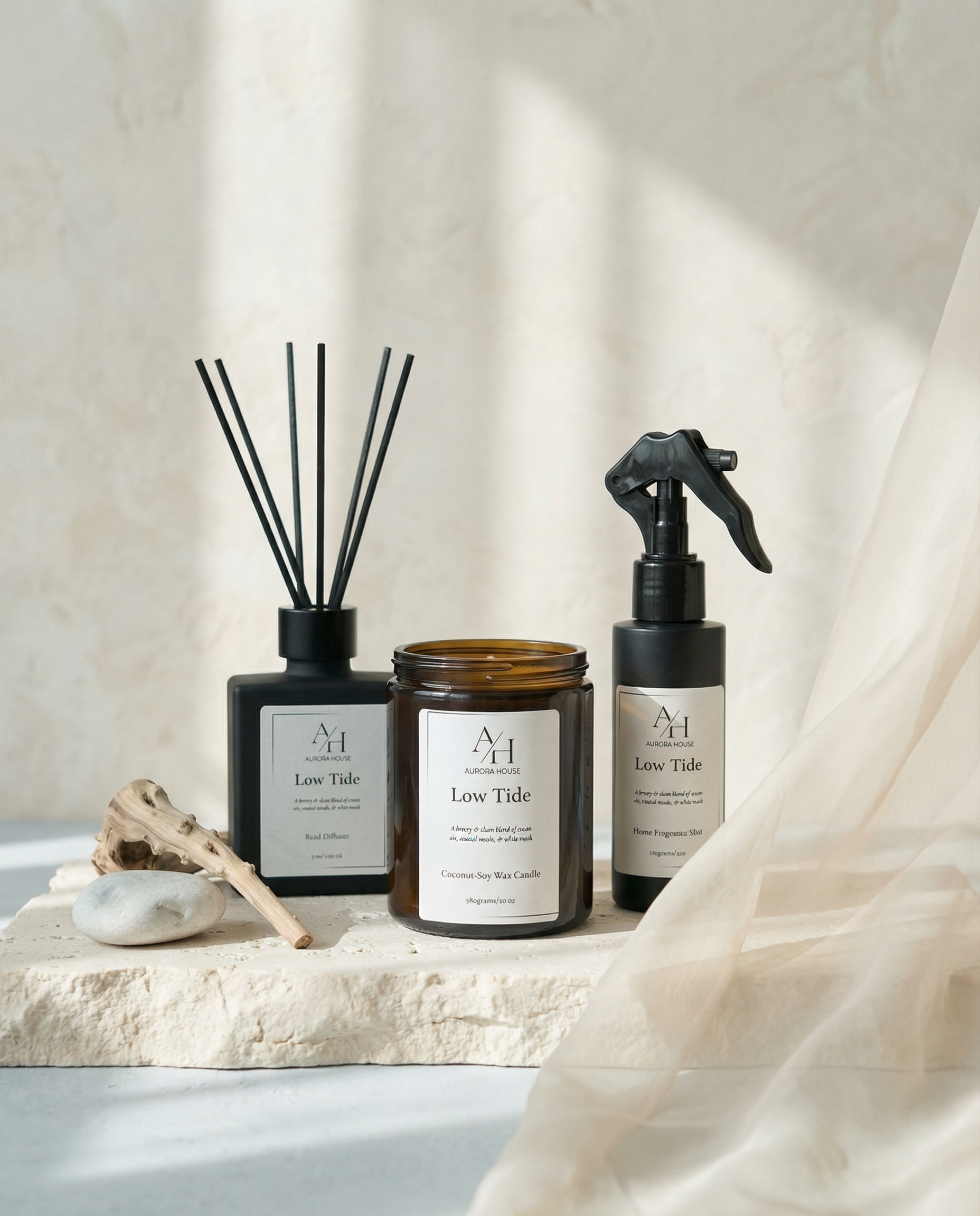 Low Tide candle, reed diffuser, and fragrance mist styled on textured stone with driftwood and coastal accents.