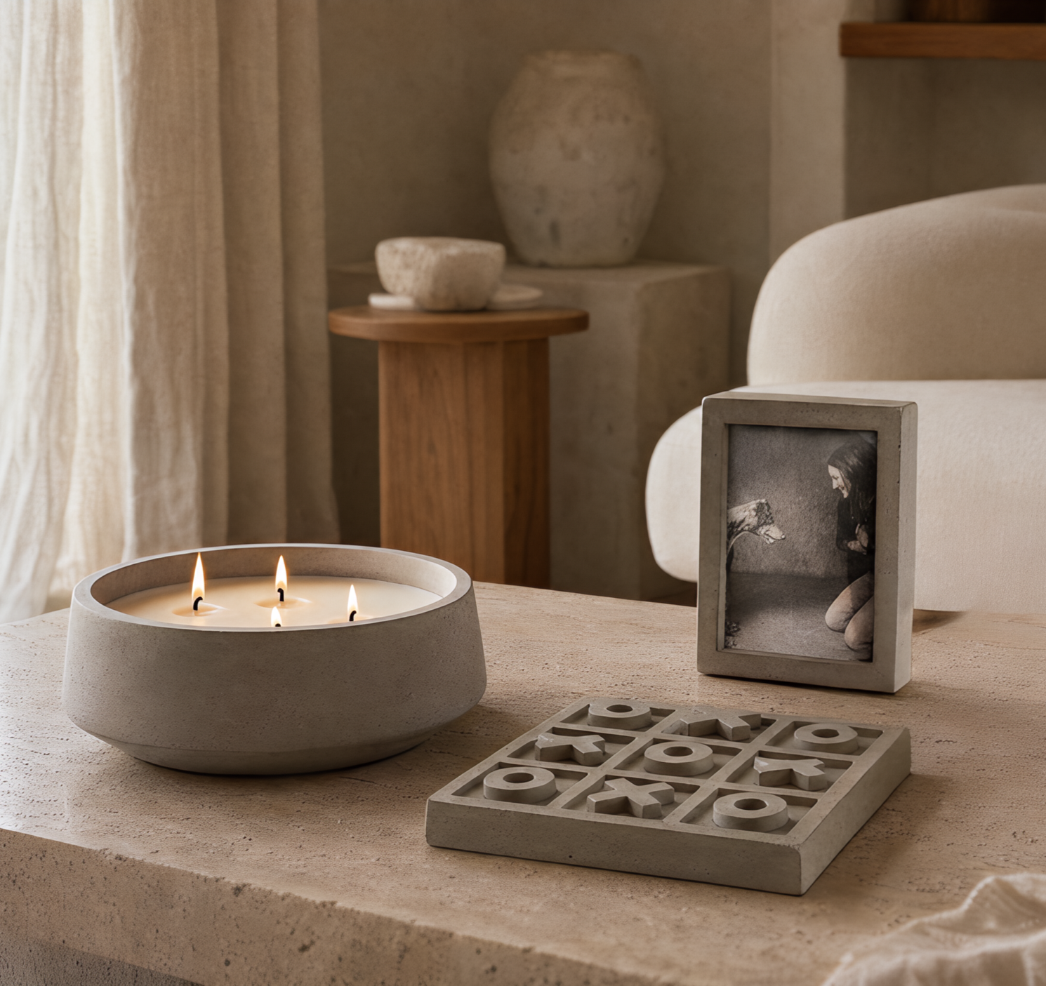 A table with a lit candle, a framed black and white photo of a woman, and a tic-tac-toe game in a cozy, neutral-colored room with decor including ceramic vases and a wooden side table.
