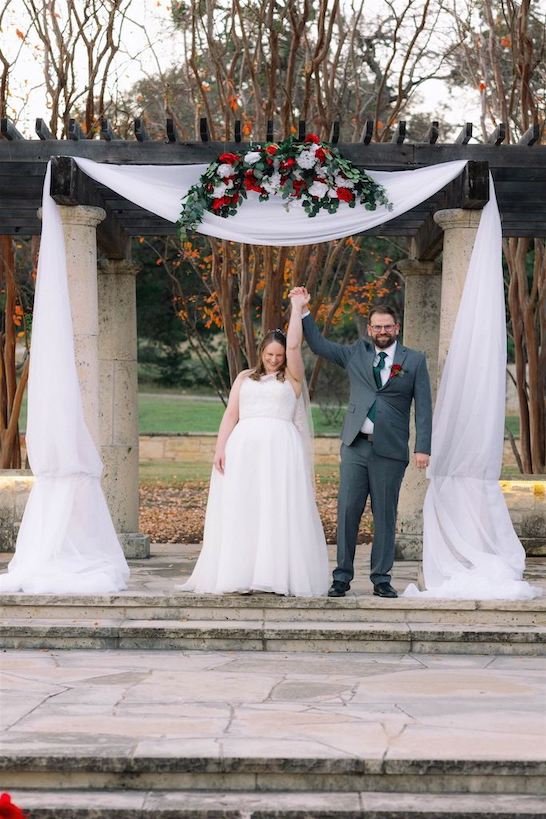 Bride and Groom Celebrating after they just got married under the Terrace at Garey House. There is Draping on the Terrace and red and White floral arrangement.