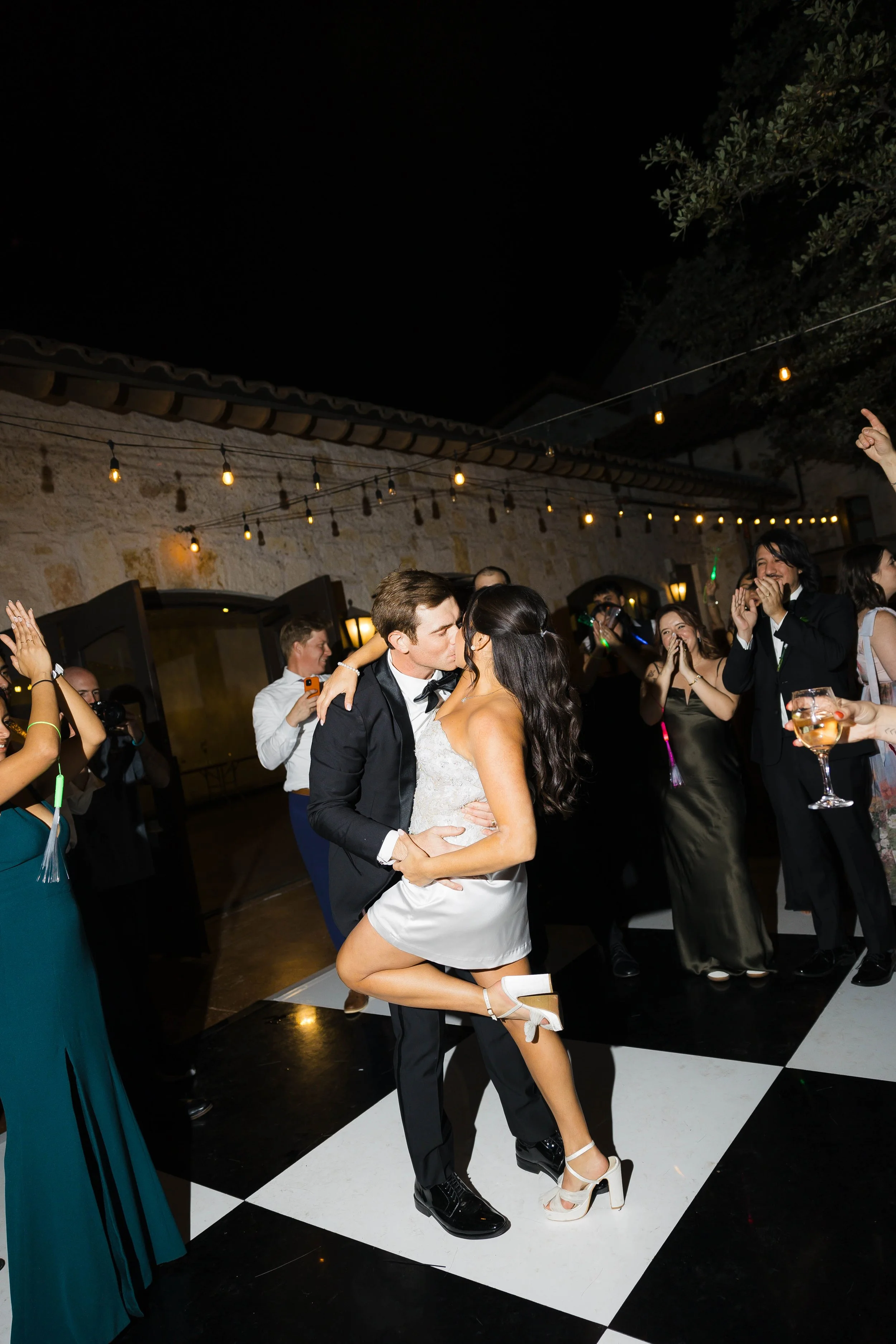 Bride wearing a short party dress and kissing her groom on a black and white checkered dancefloor