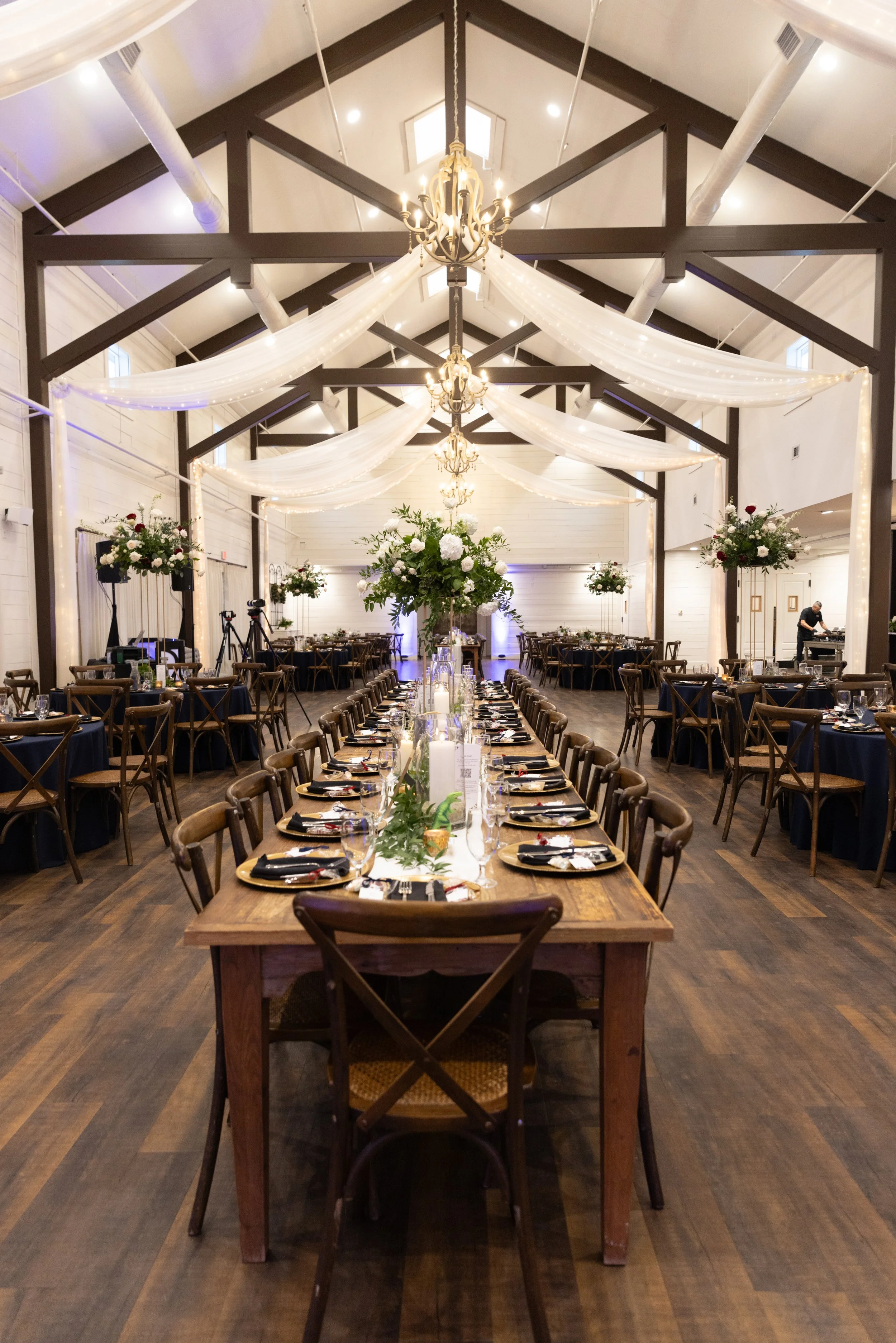 Long wooden tables with Tall flower arrangements during a wedding reception