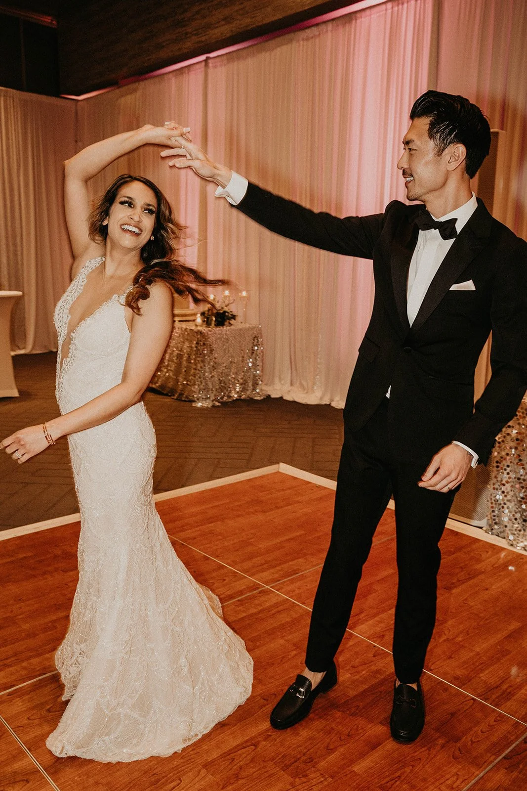 Bride and Groom dancing in a ballroom with Pink Uplights and wooden dancefloor