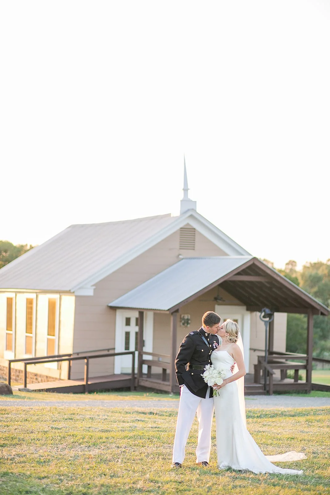 Couple kissing by a small intimate church in the Texas Hill Country and groom in his military uniform