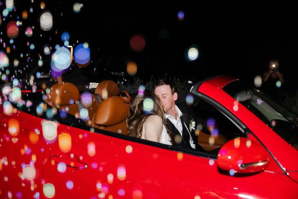Couple kissing in a red getaway car after their wedding and bubbles in the air at HighPointe Estate in Georgetown Texas