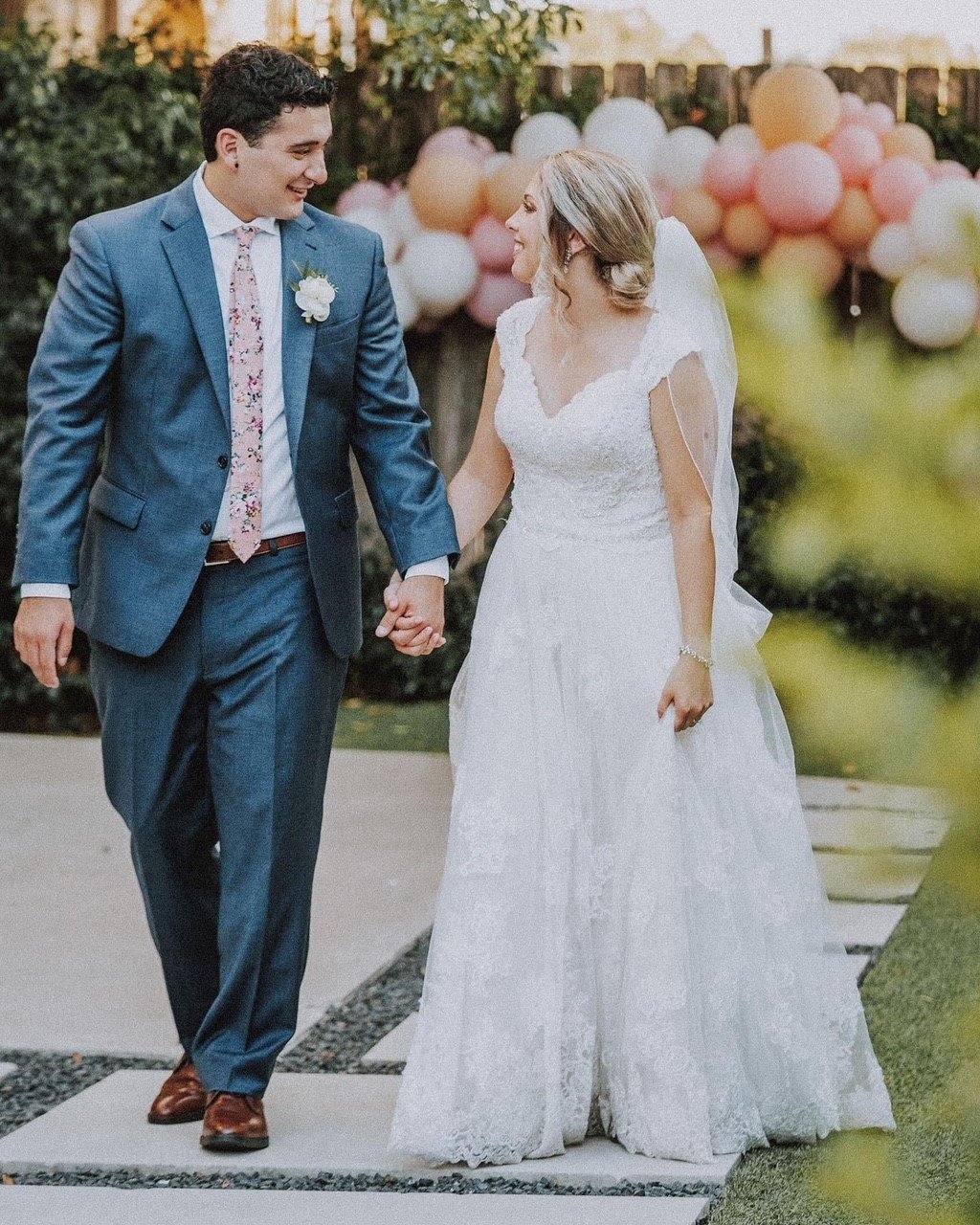 Couple walking and holding hands with Groom in a blue suit and pink accents