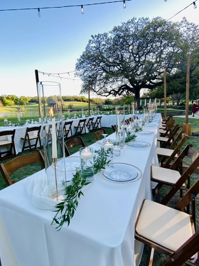 Long guest tables in a U-shape with string lights going across the tables on the lawn by the pond at Garey House
