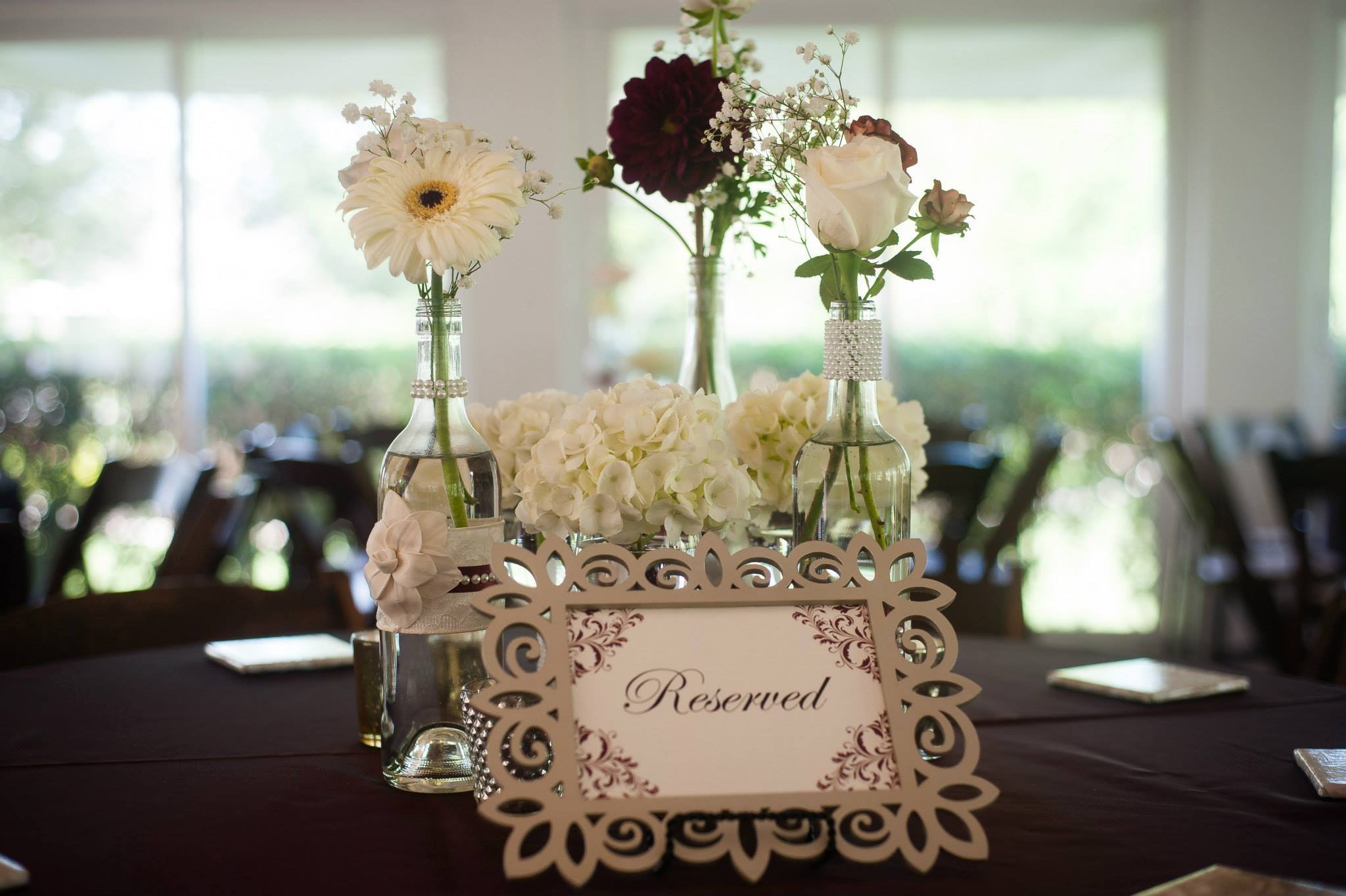 Wooden cutout reserved sign on a reception table with Wine Bottle decor and maroon linens