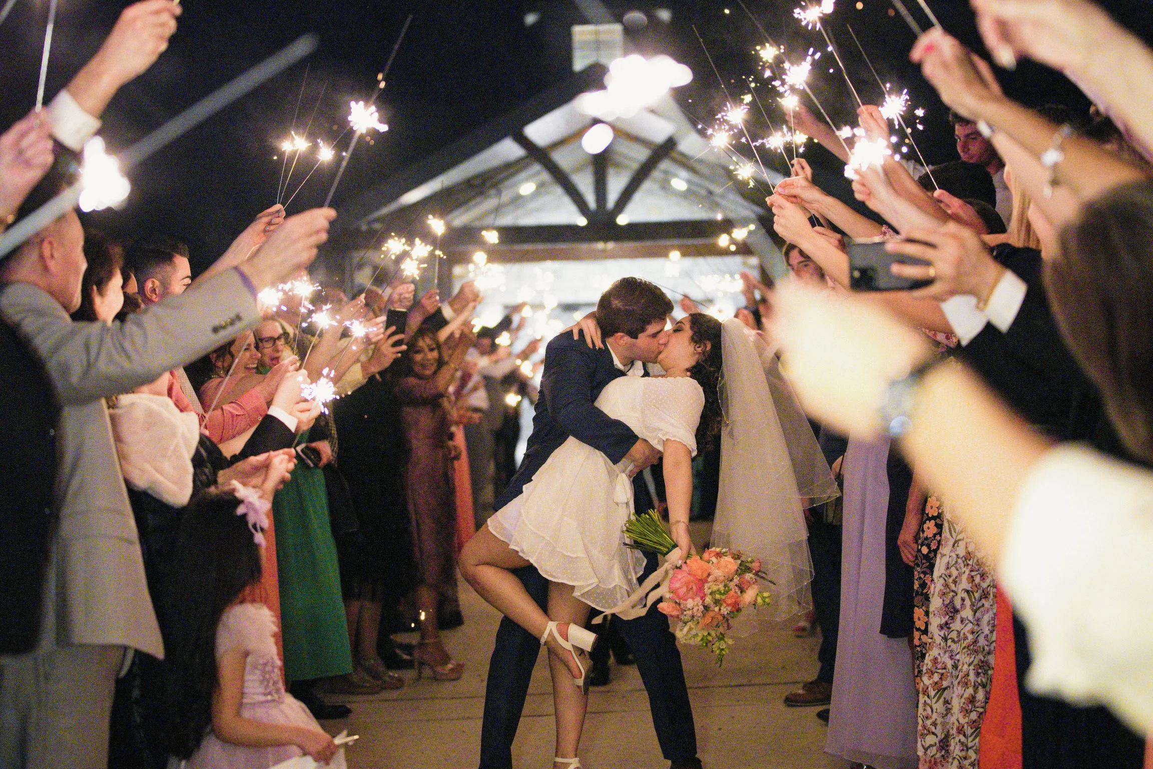 Couple kissing during a sparkler exit while the bride is in a short wedding dress and veil at HighPointe Estate