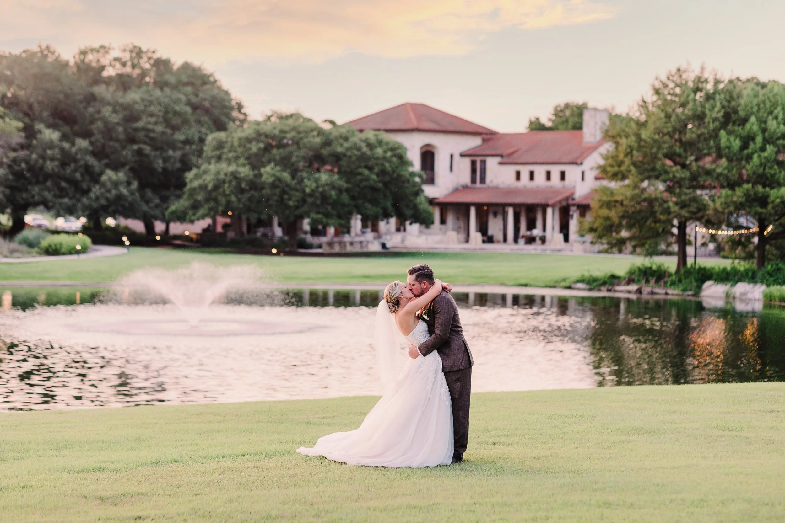 Couple kissing in field in front of pond at Garey House in Georgetown Texas
