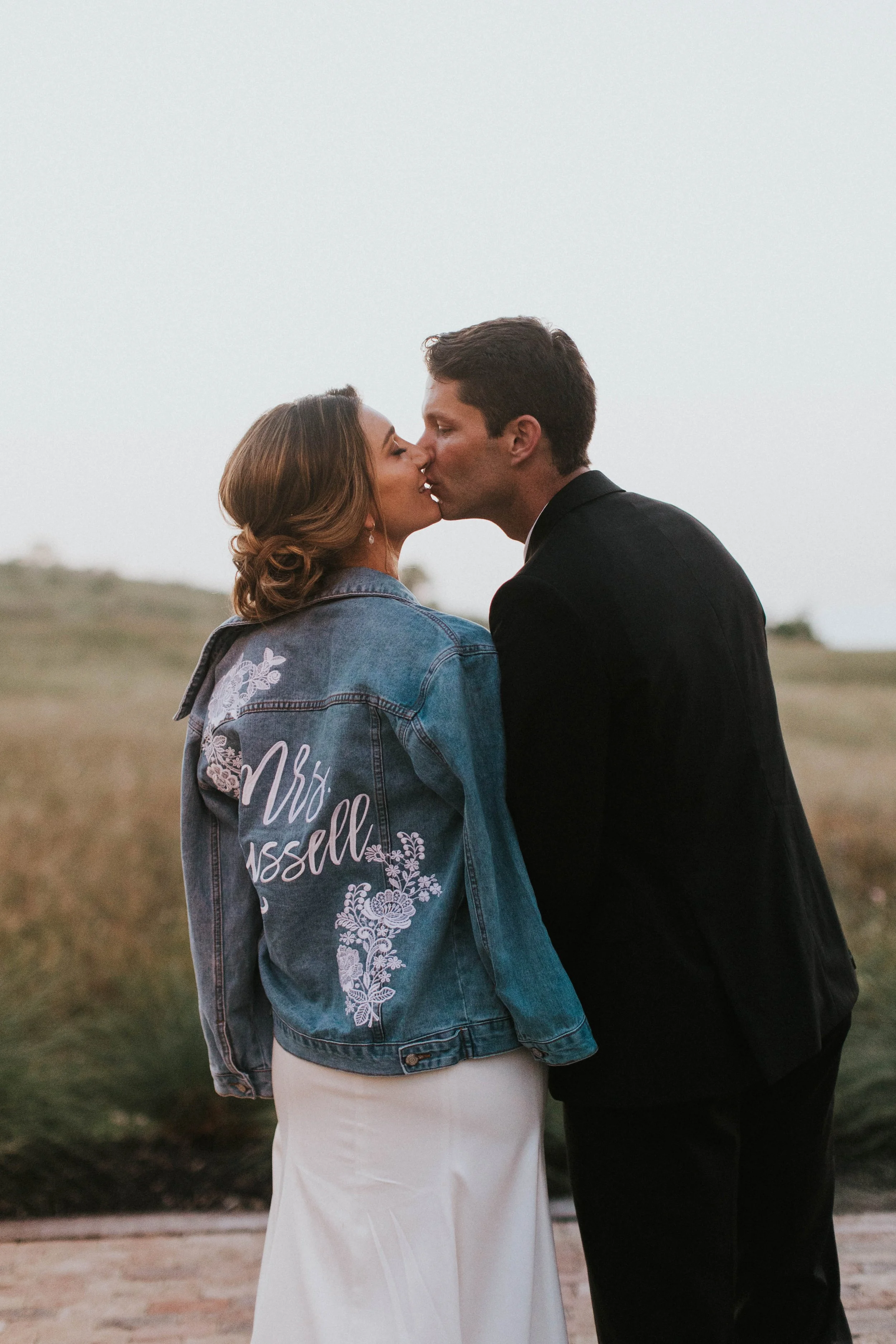 Bride and Groom Kissing and Bride wearing a personalized jean jacket at Two Wishes Ranch in Lockhart Texas