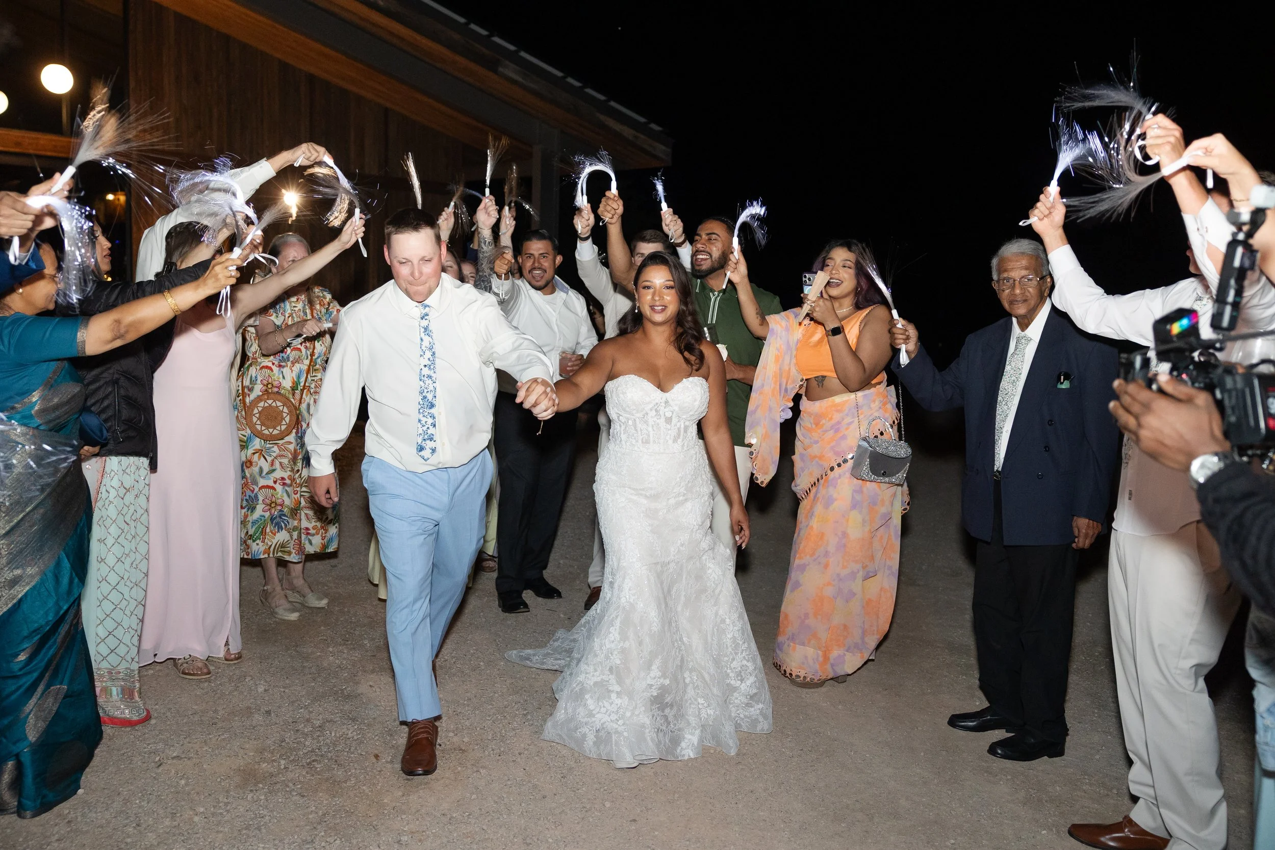 A bride and groom holding hands in the center, surrounded by friends and family celebrating at night with party sparklers during their grand exit from their wedding at Walden Retreats.