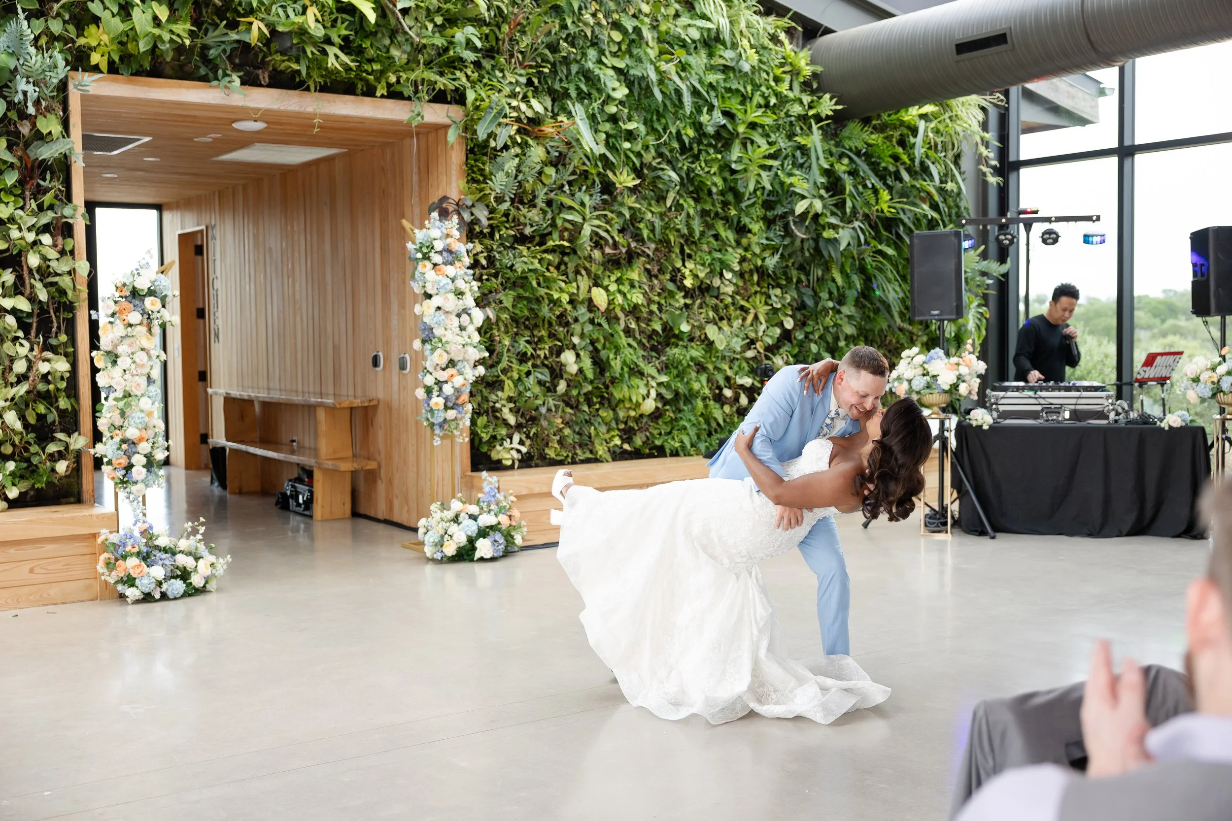 A bride and groom dancing at their wedding reception with a green flower wall and DJ in the background at Walden Retreats.