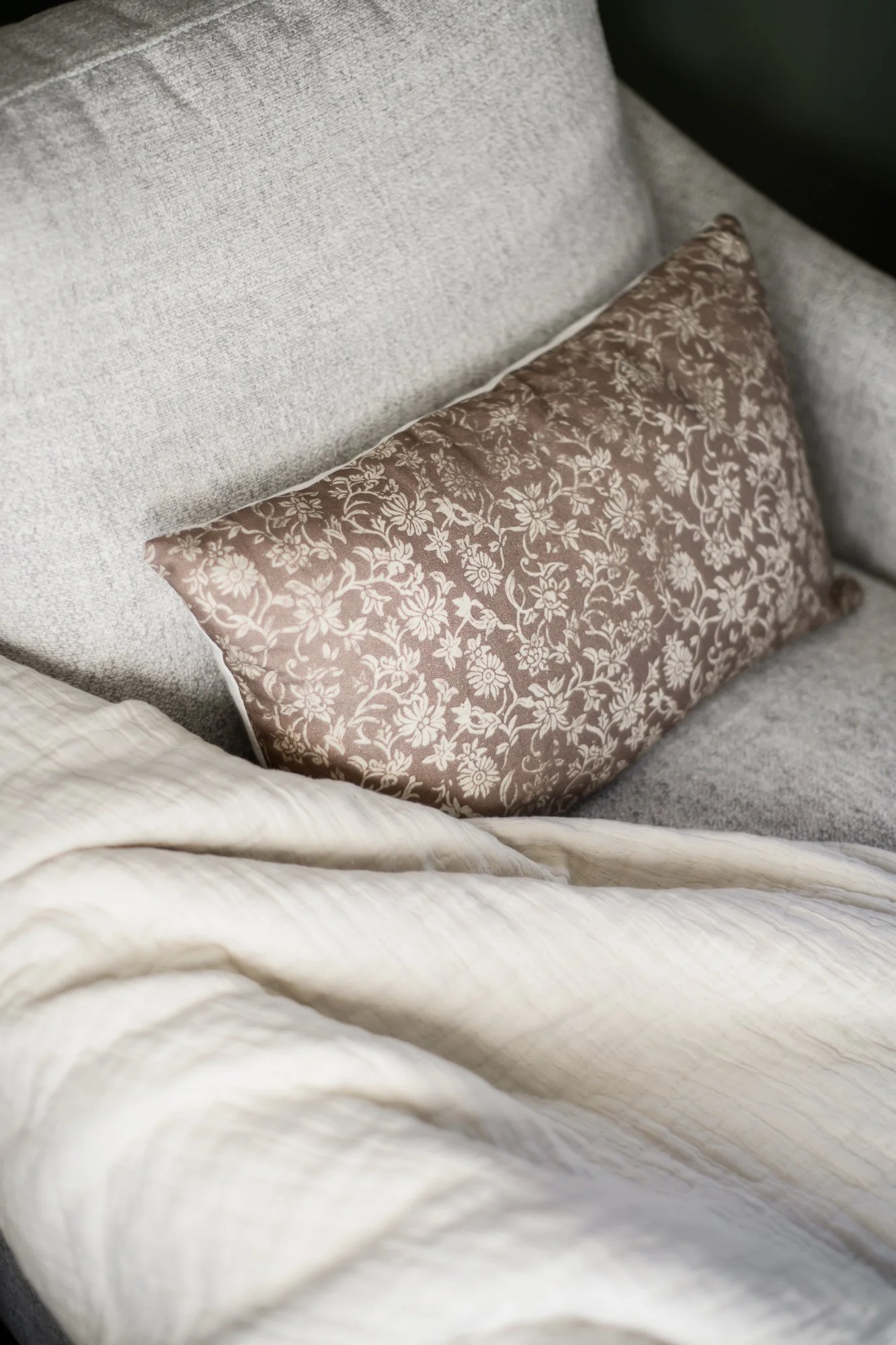 Close-up of a bed with a beige fabric headboard, a patterned brown pillow, and cream-colored bedding.