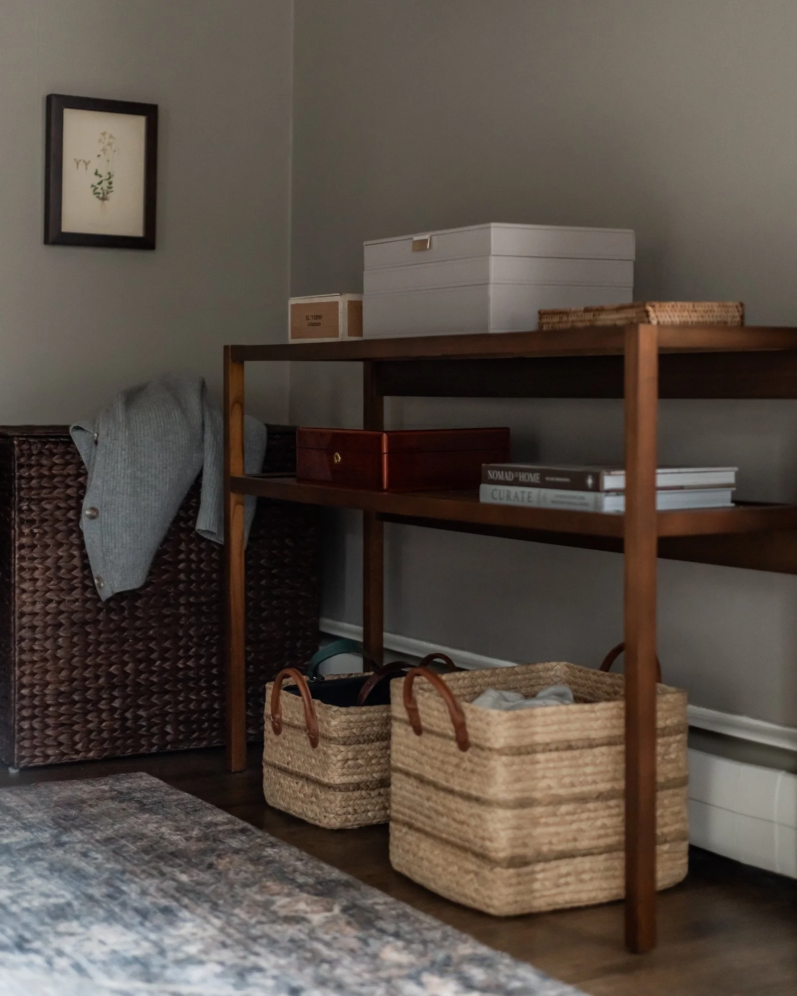 Wooden shelf with storage boxes, woven baskets on the floor, a wicker cabinet, and a wall picture in a cozy room.