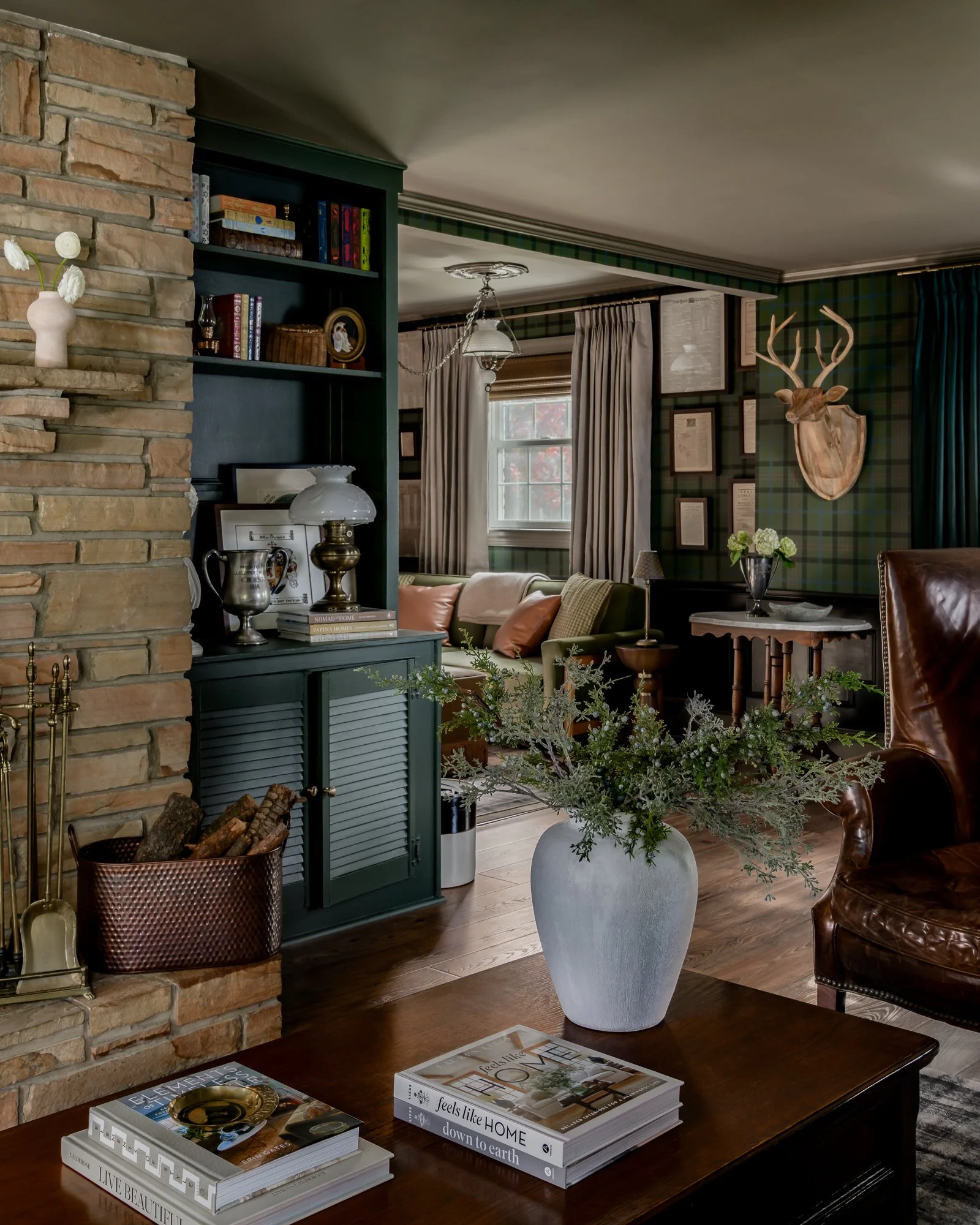 Living room with a brick fireplace, blue bookshelf, and a wooden coffee table with a white vase of greenery and books.
