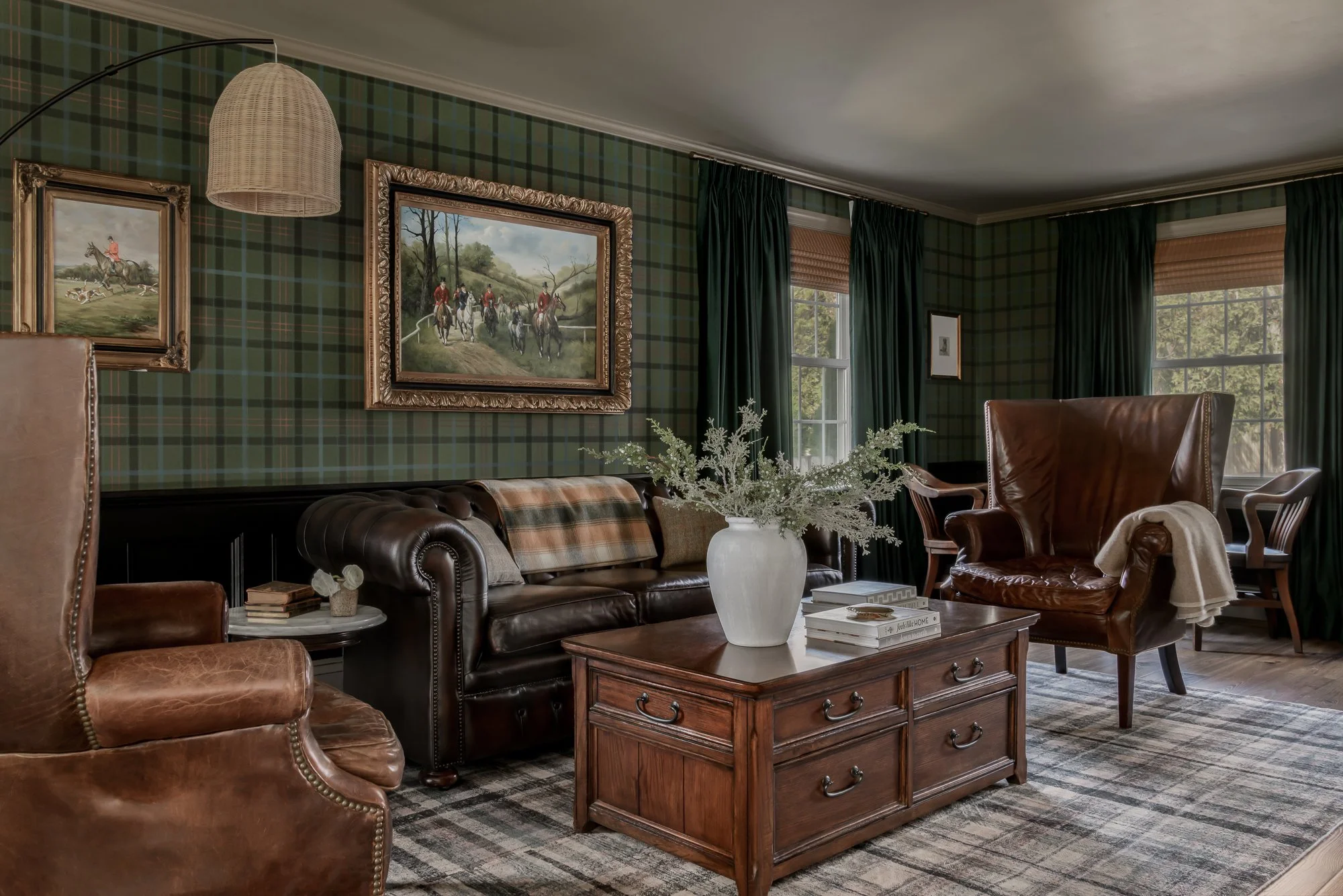 Living room with green plaid wallpaper, leather armchairs, a wooden coffee table with a large white vase, and framed paintings of fox hunting scenes on the wall.
