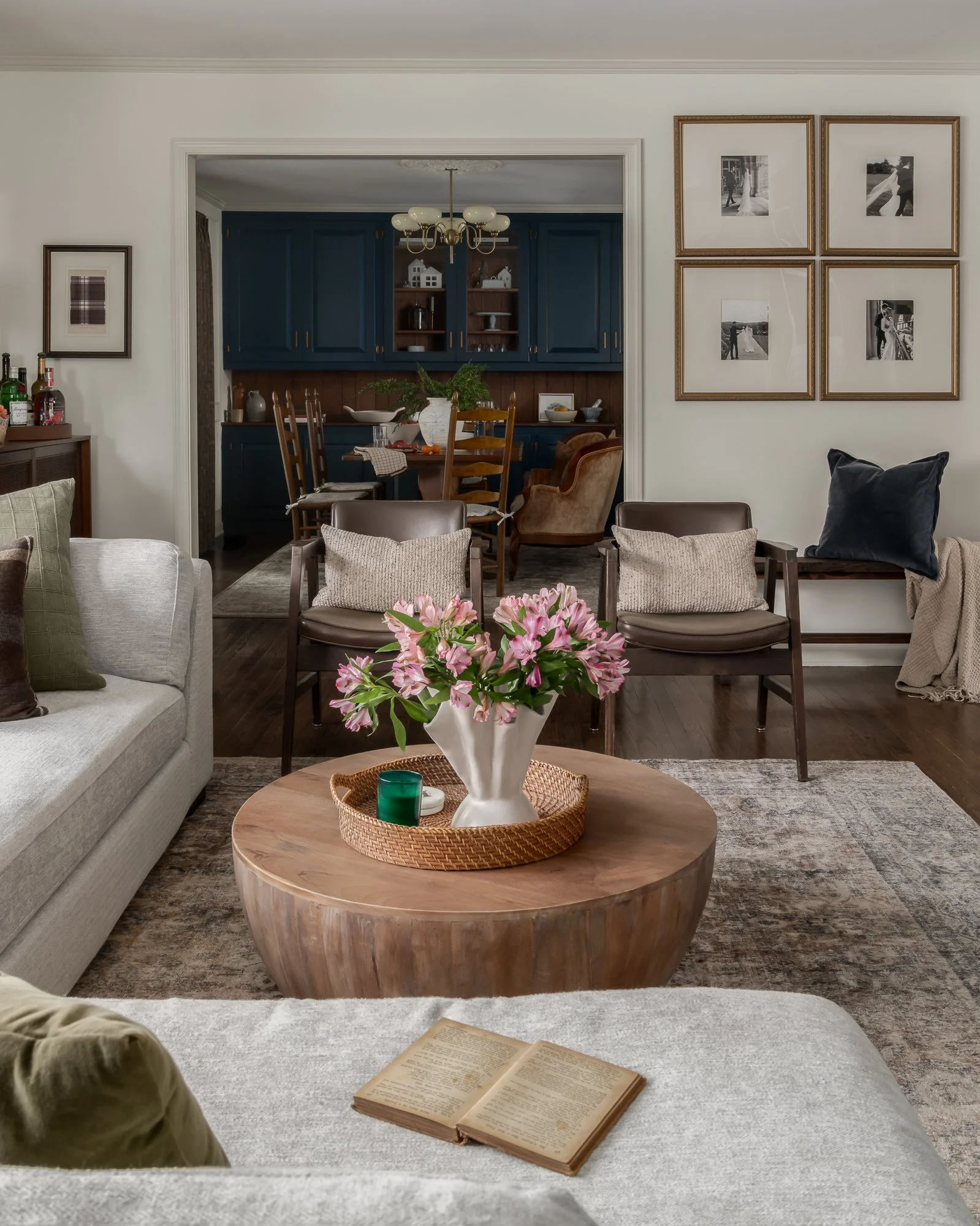 Living room with floral centerpiece on coffee table, view of dining area in the background, wall art, and decorative pillows.