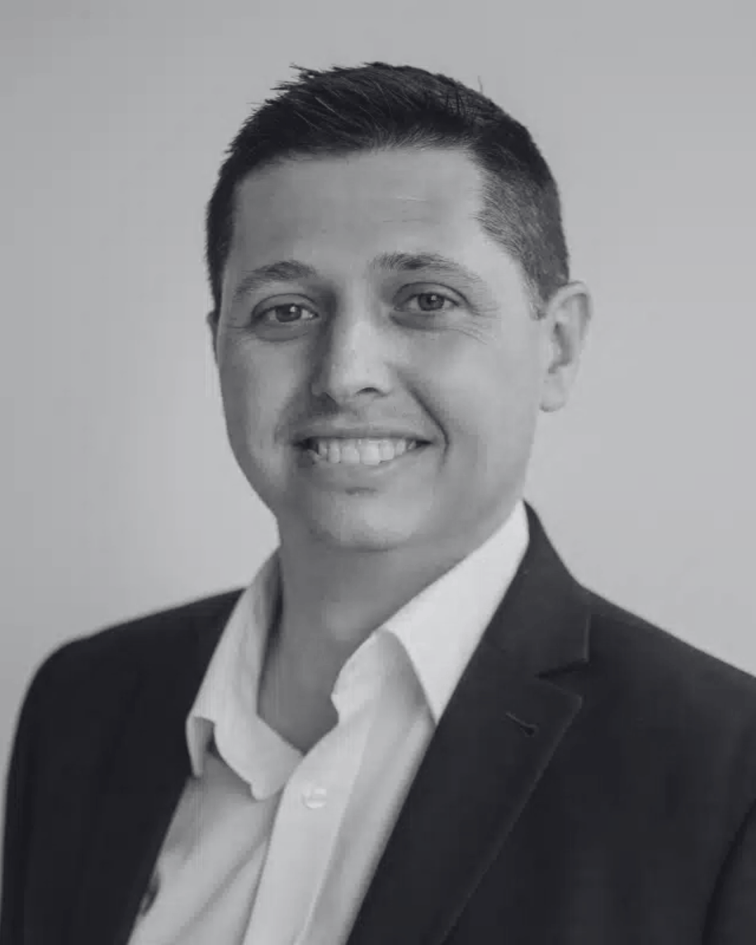 Black and white professional headshot of a smiling man, steven kenny, wearing a suit jacket and white collared shirt.