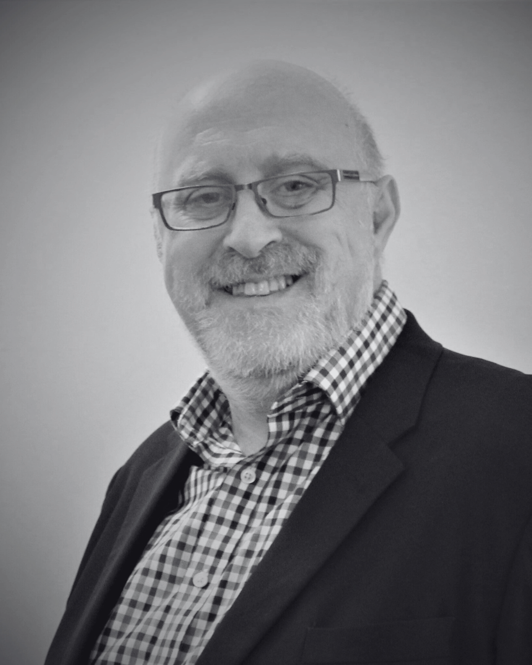 Black and white photo of a smiling middle-aged man, mike hurst, with glasses, a beard, a checkered shirt, and a dark blazer.