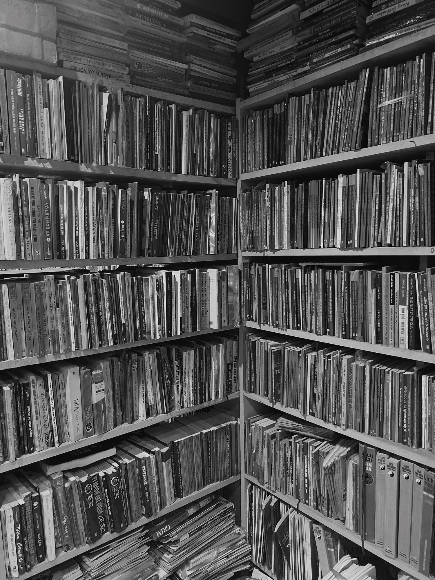 Bookshelves filled with numerous books and magazines, arranged in no specific order, in a room with wooden shelves.