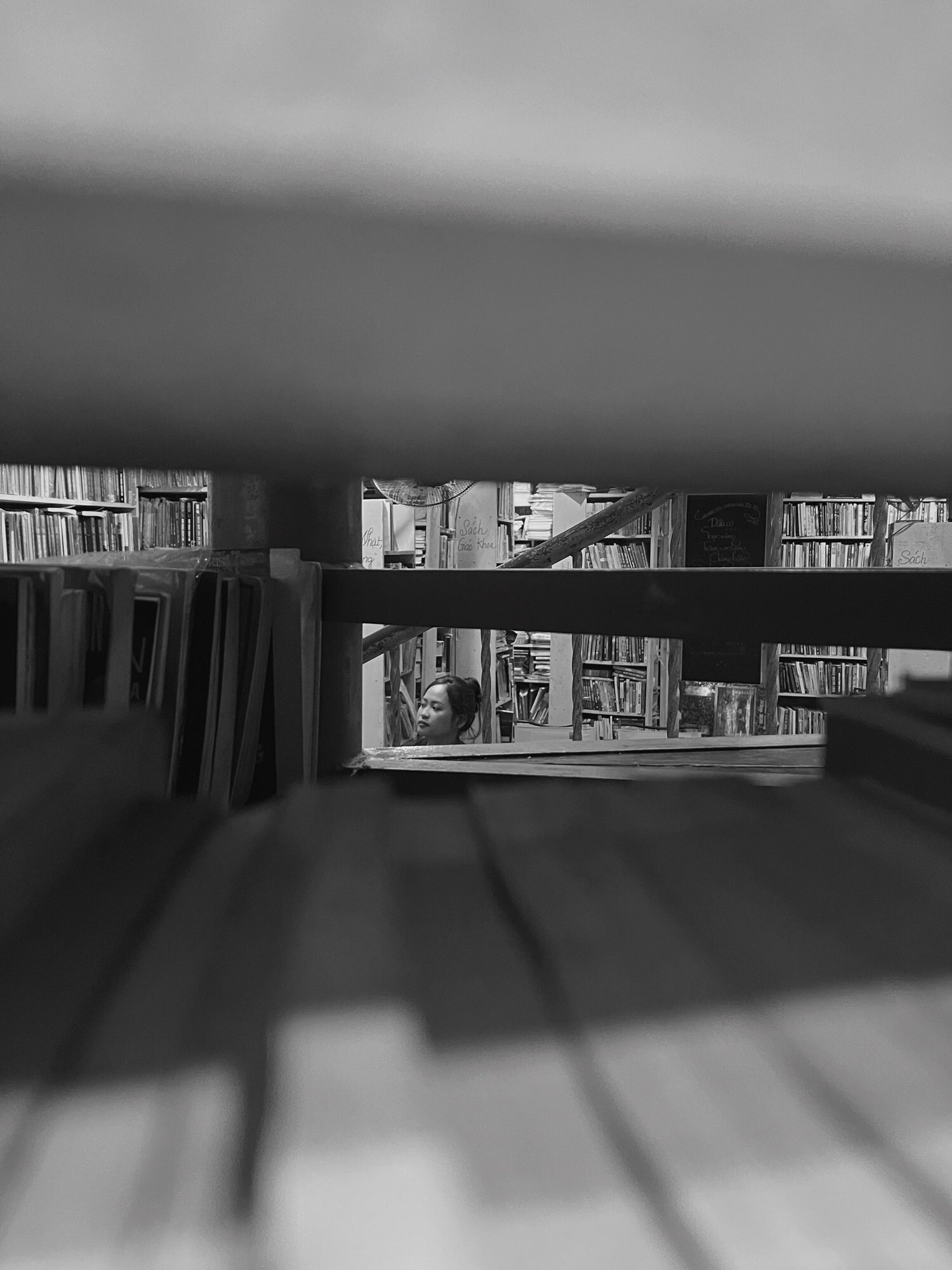 A person's face and shelves of books in a bookstore, seen through the gaps of a wooden structure.